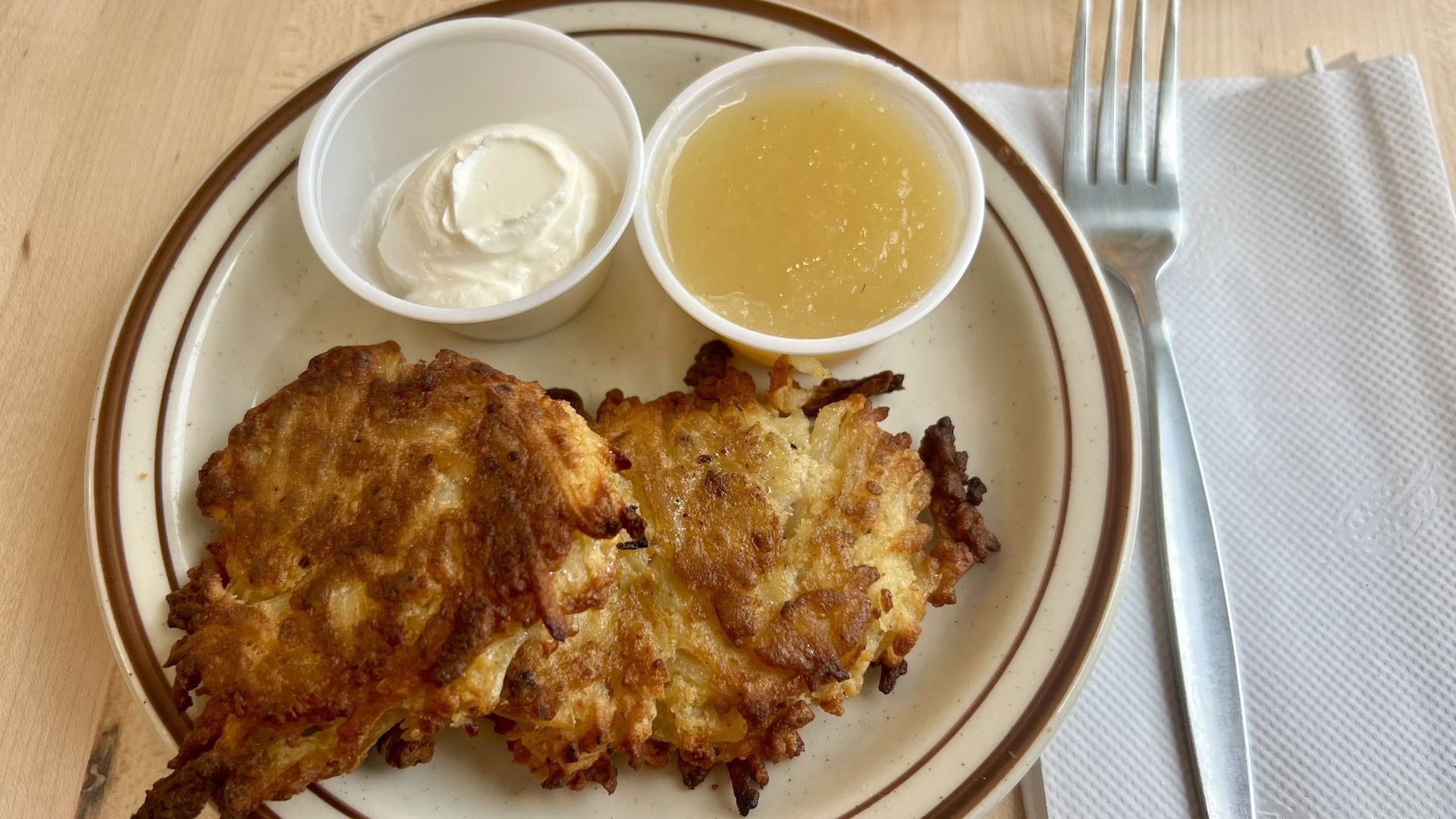 Potato pancakes on plate with cups of sour cream and applesauce with plastic fork next to plate.