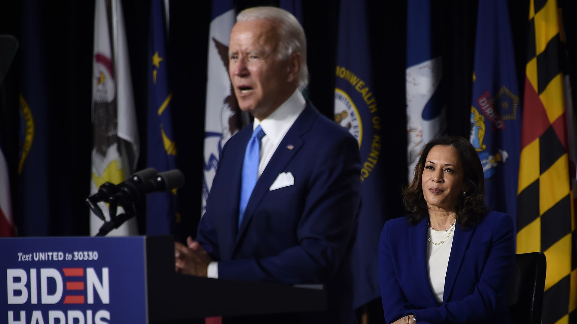 Kamala Harris watches Joe Biden speak at a podium 