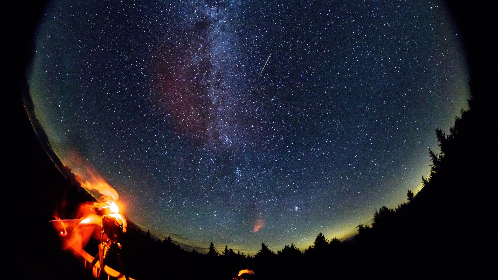 A photographer watches the clouds of the Milky Way and a meteor overhead