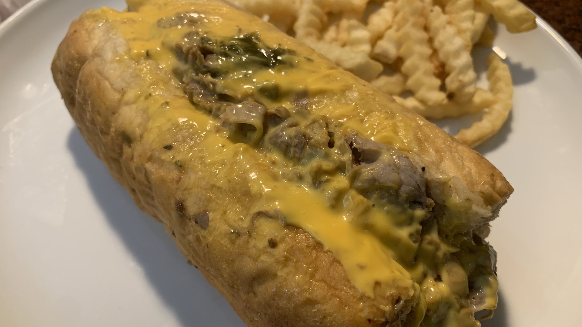 Photo of a cheesy sandwich on a plate next to fries 