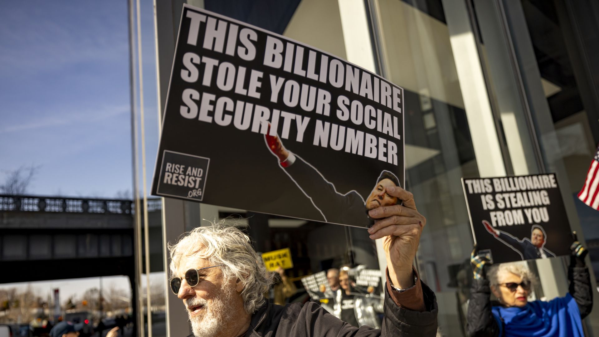 A protester holds signs that read: "This billionaire stole your social security number" during a protest at a Manhattan Tesla dealership