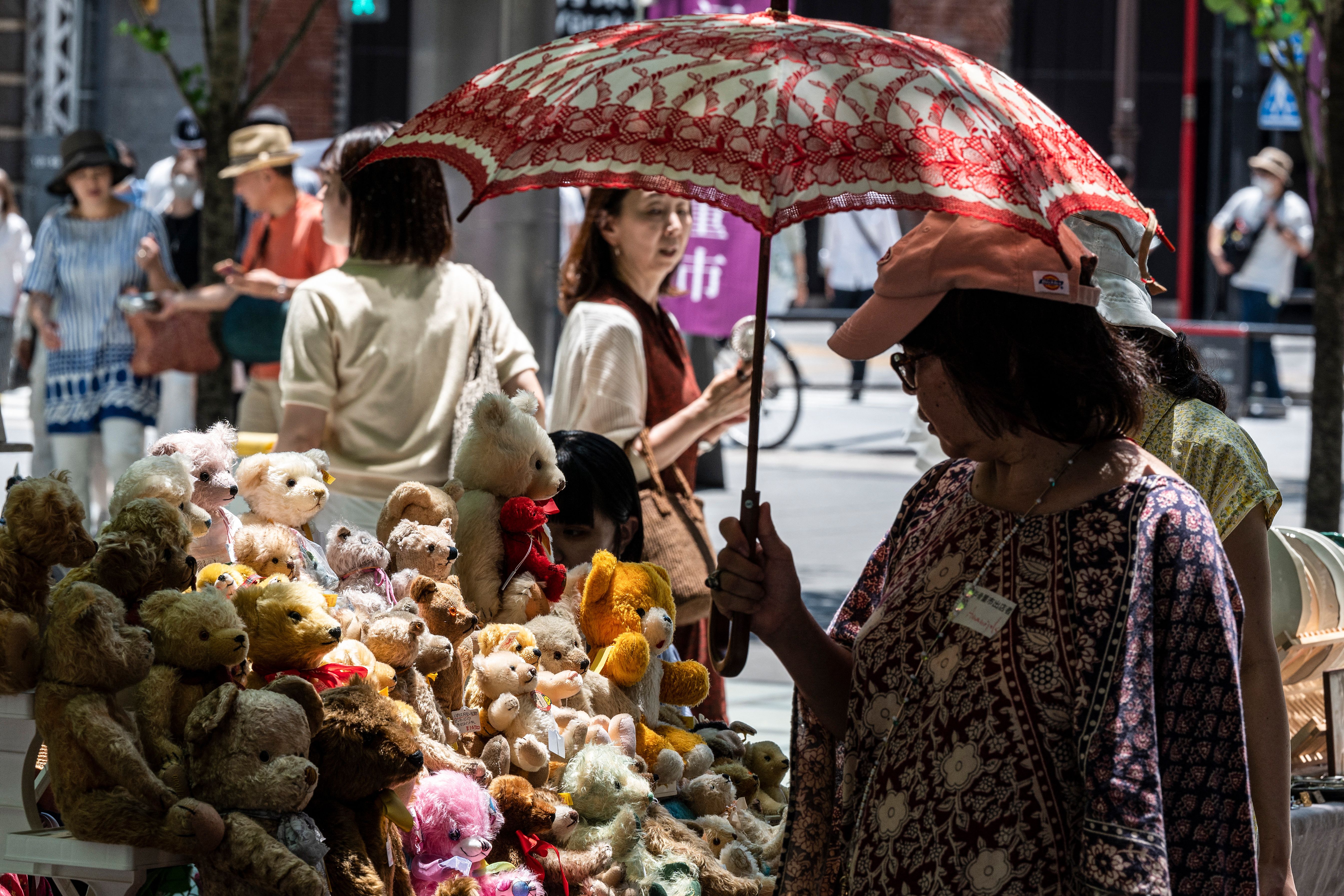 A woman (R) uses an umbrella to shelter from the midday sun as she looks Teddy Bears for sale at an outdoor antique market in downtown Tokyo on July 17, 2023. 