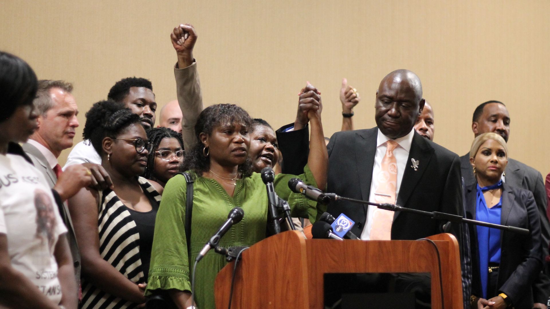 Photo of a woman in green holing hands with a man in the air, as others join with raised fists above their head. 