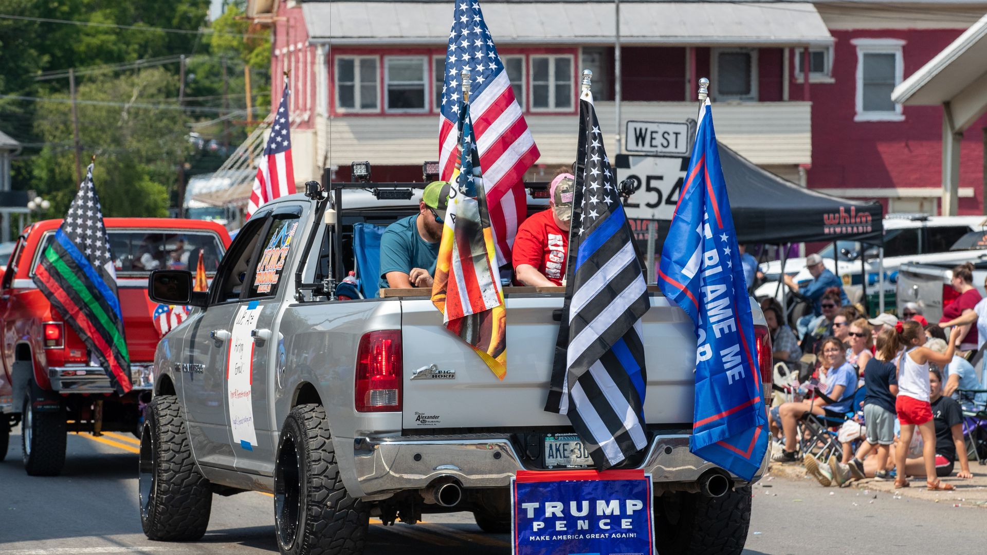 A pickup truck with various flags and a Trump-Pence election sign drives on the street during the Independence Day parade. 