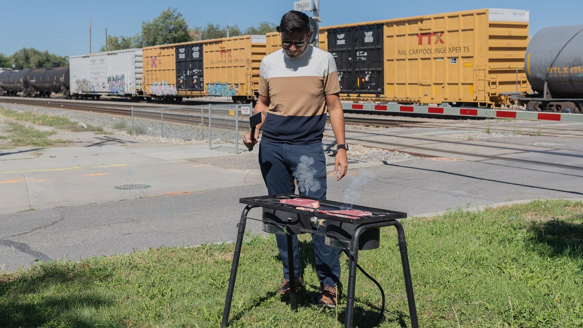 A man grills steaks in front of a stopped train.