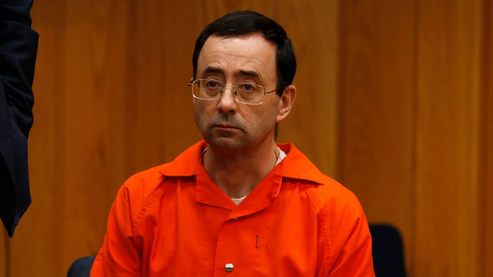 Larry Nassar in orange jumpsuit looks sad.