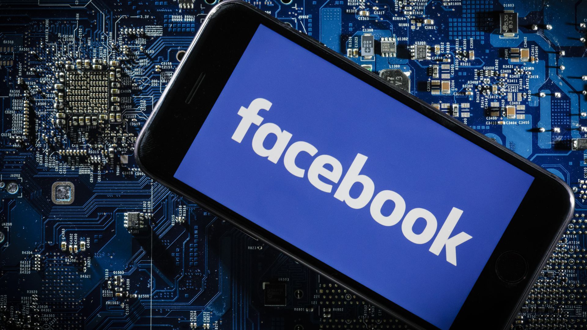 A phone with the Facebook logo set against a circuit board.