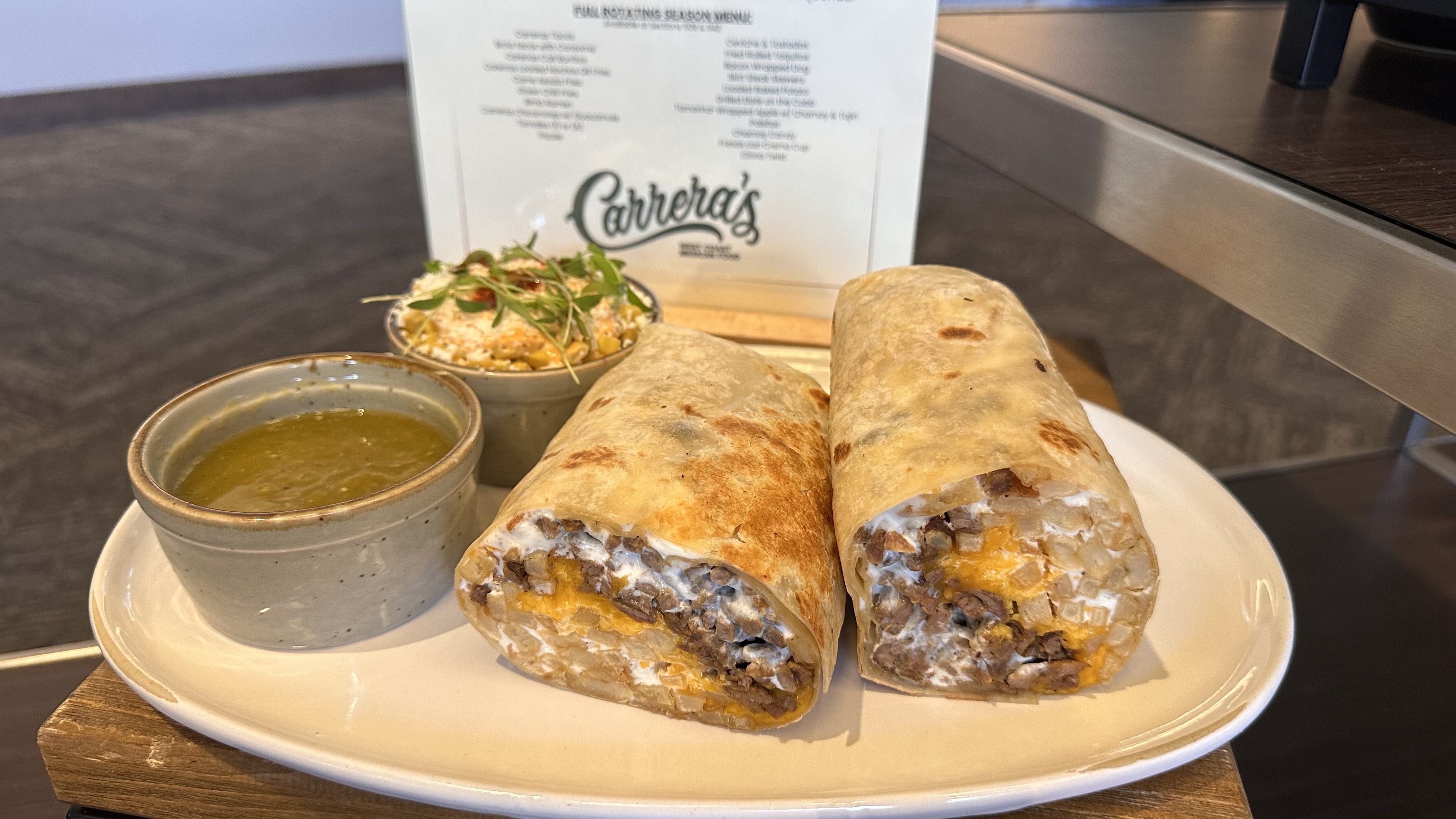 Two beef-and-cheese burritos cut open on a white plate, with a side of green sauce and a small salad cup; a "Carreta's" menu card stands in the background.