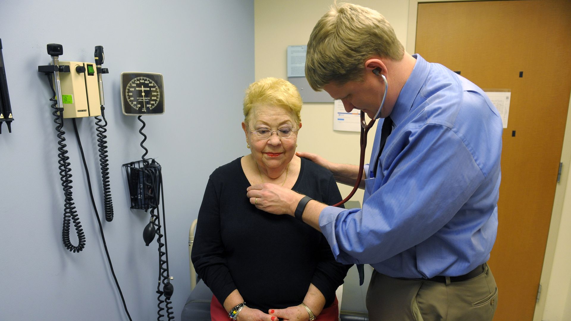 A doctor listens to the heartbeat of a patient in an exam room.