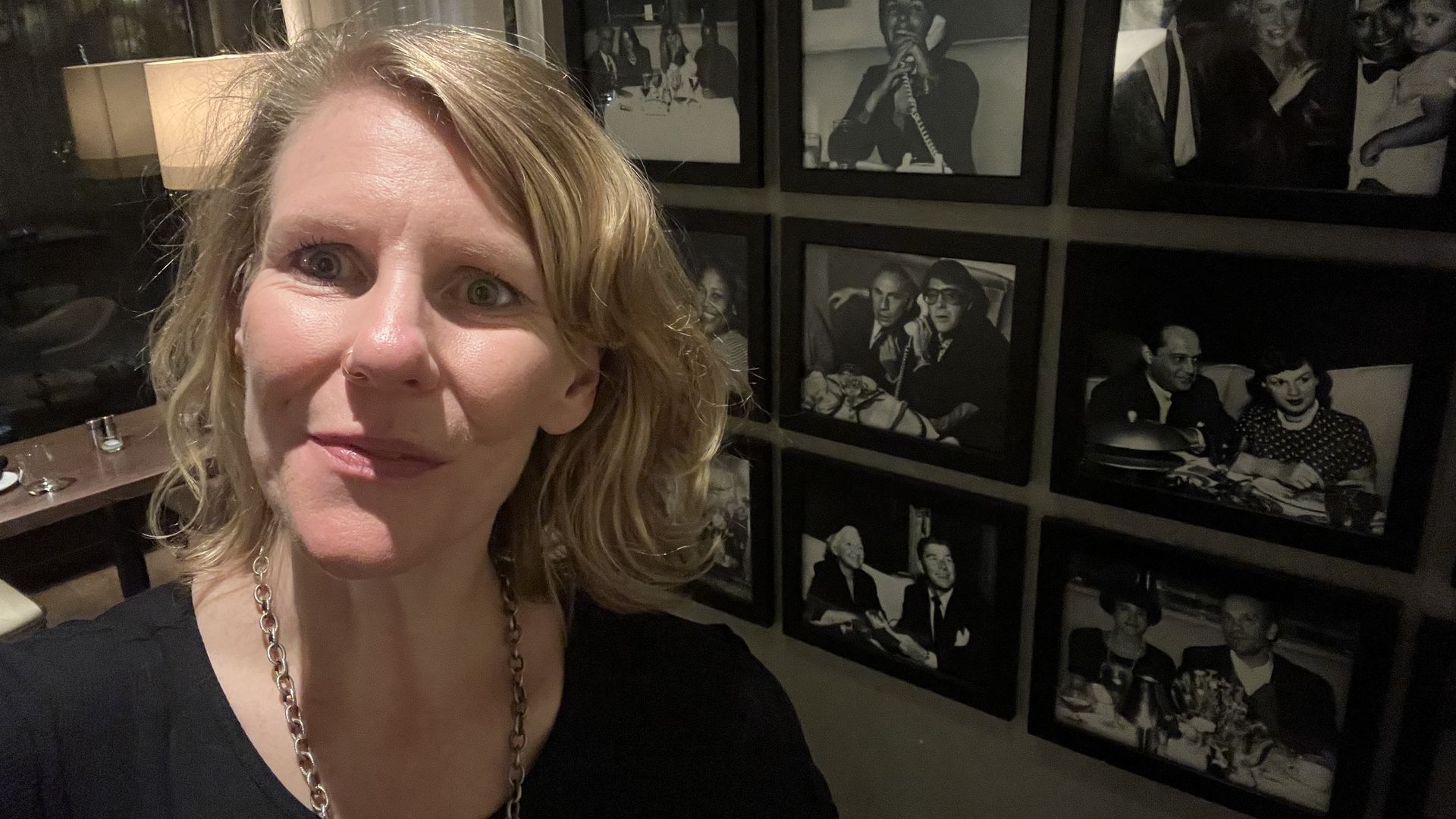 Woman in black shirt standing in front of a wall of photos.