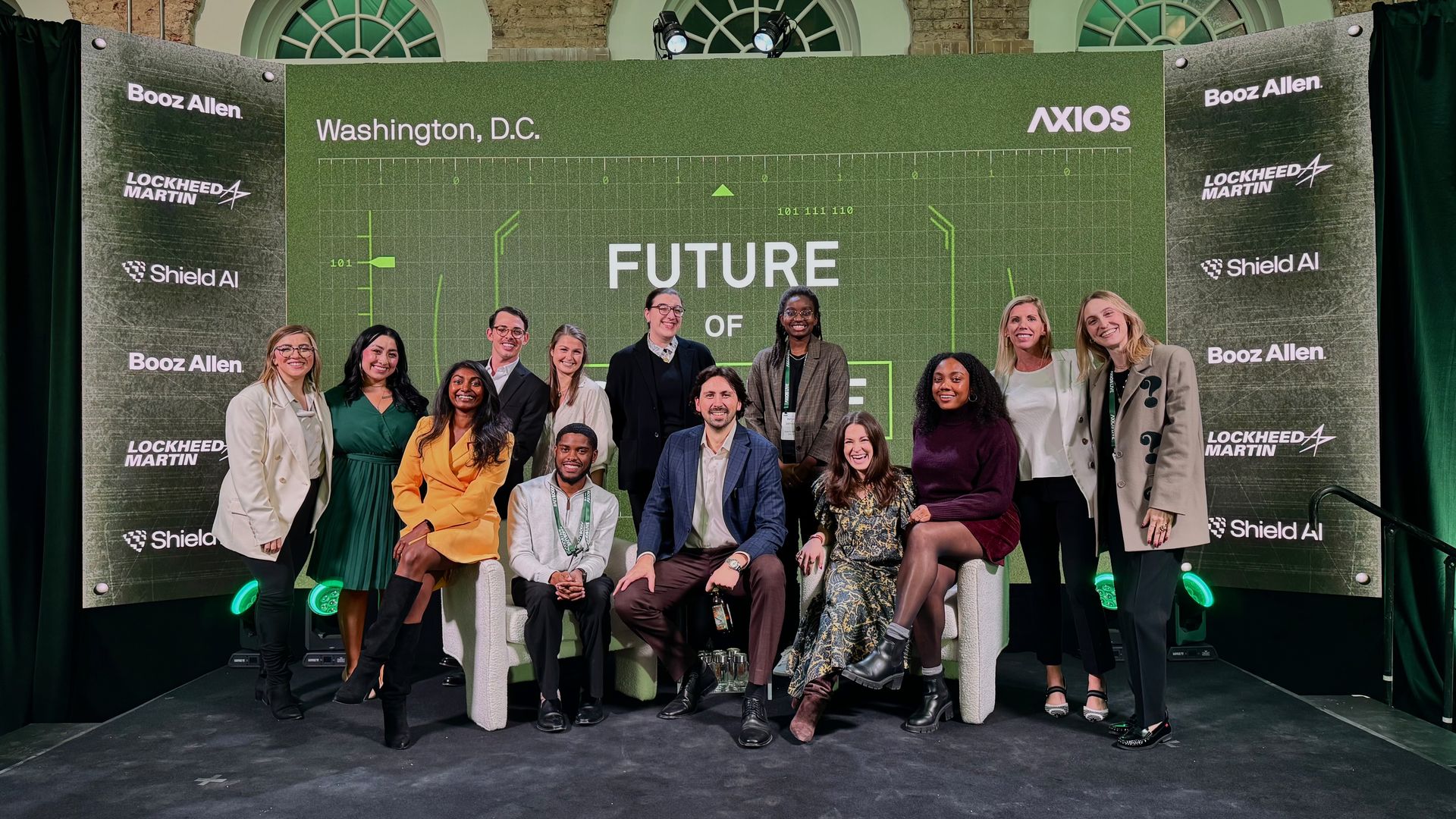 Group of professionals posing on stage with a green backdrop displaying "FUTURE OF" and logos for Booz Allen, Lockheed Martin, Shield AI and Axios in Washington, D.C.