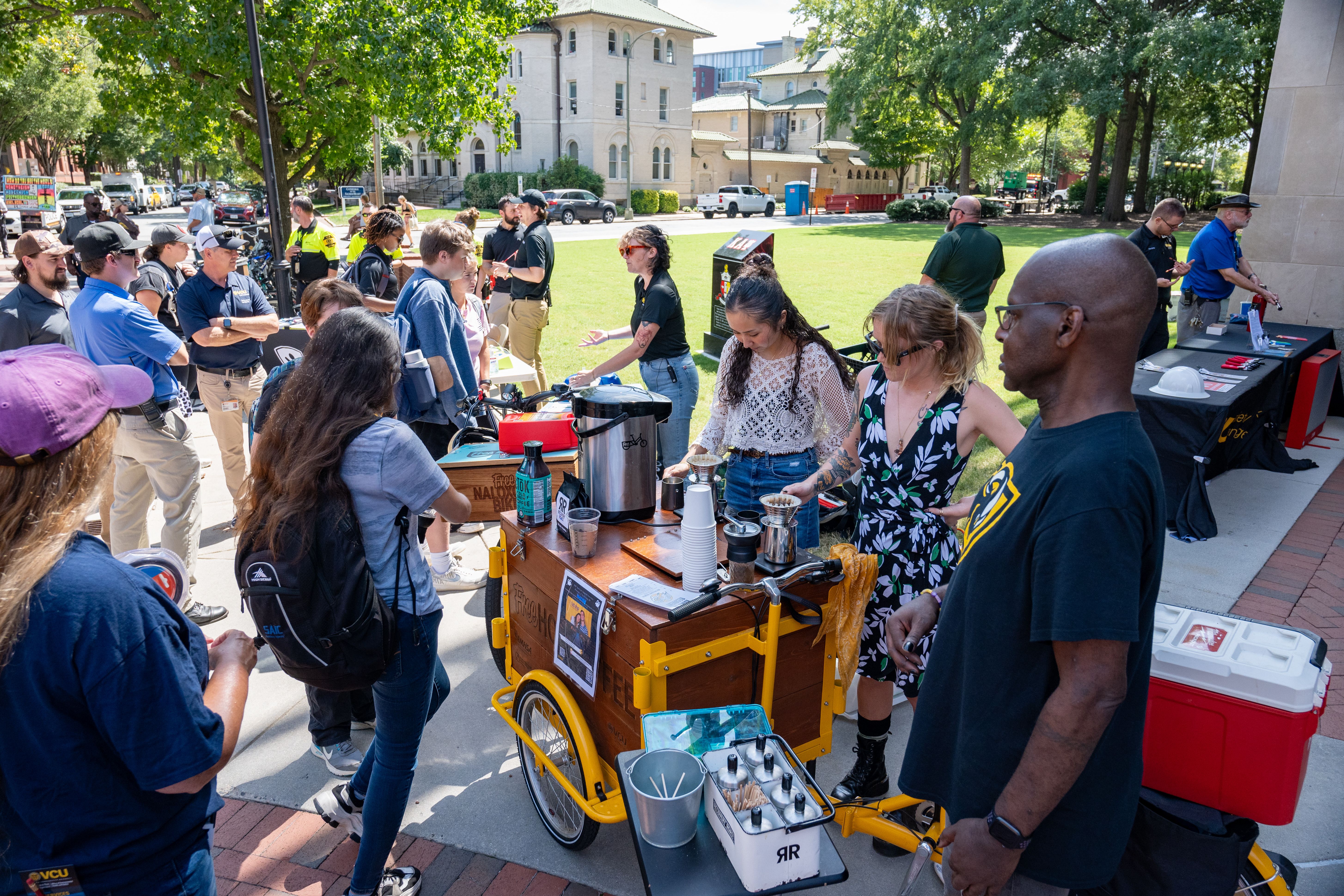 a crowd of people around a coffee cart and a bike that has a wooden crate saying "free naloxone bike"