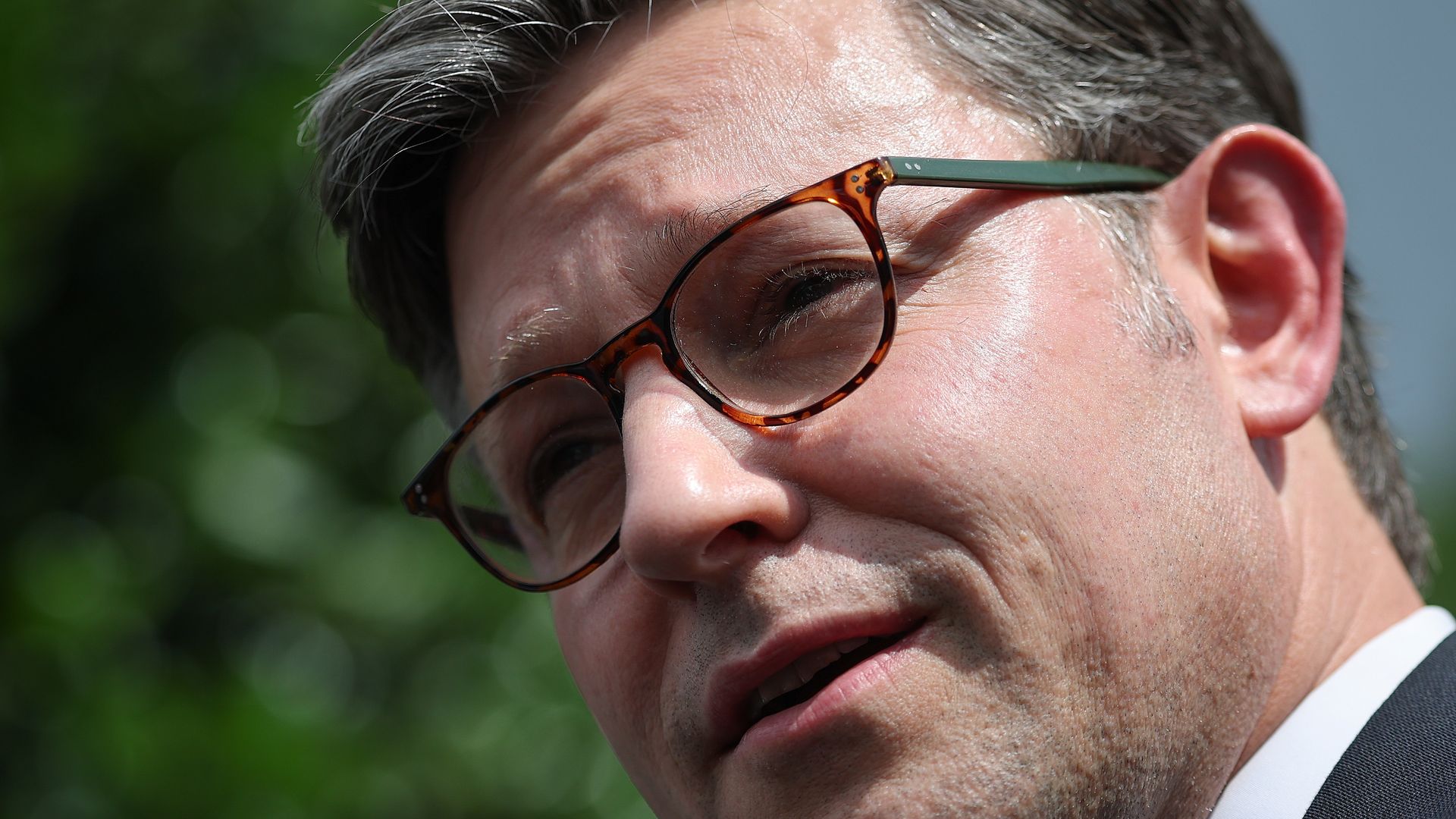 House Speaker Mike Johnson, wearing a gray suit and standing in front of a tree.