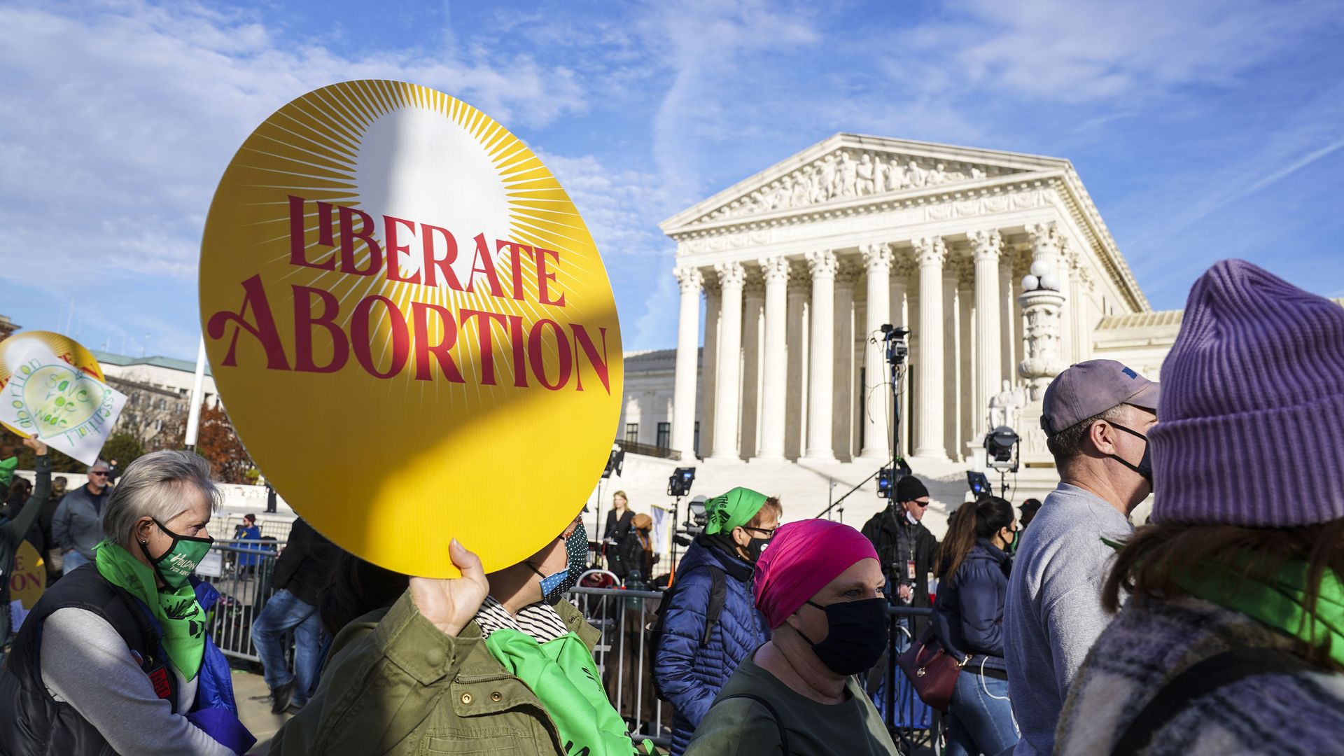 Picture of pro-choice advocates marching in front of the Supreme Court, one is holding a sign that says "liberate abortion"