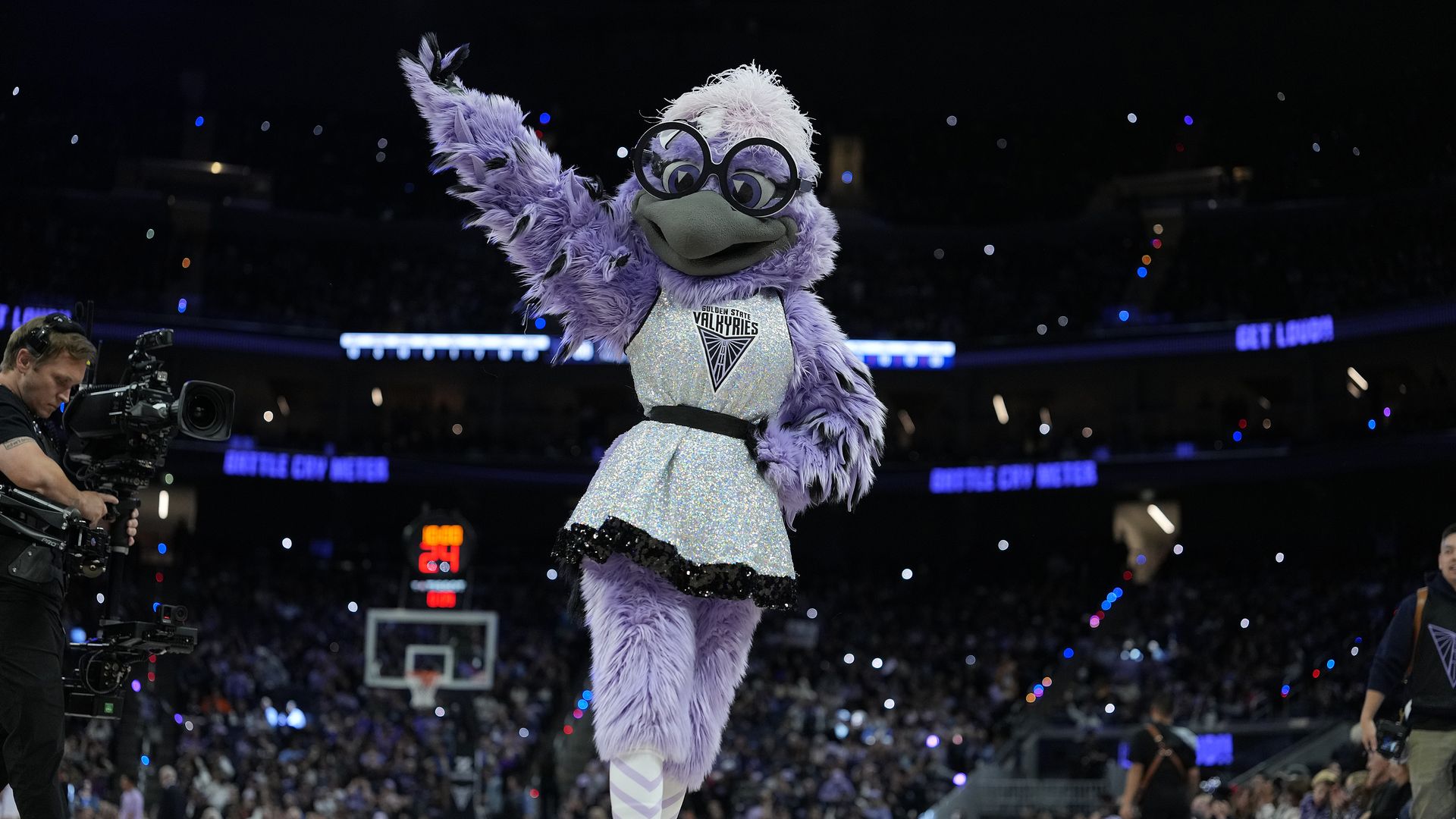 The Golden State Valkyries mascot "Violet," a giant purple bird mascot wearing glasses, stands on the arena floor wearing her Valkyries uniform. 