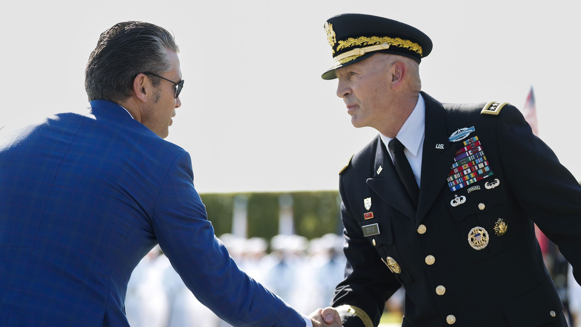 Randy George, wearing a dark military uniform covered in pins and badges, shakes hands with Defense Secretary Pete Hegseth, who is wearing a blue suit jacket and sunglasses.