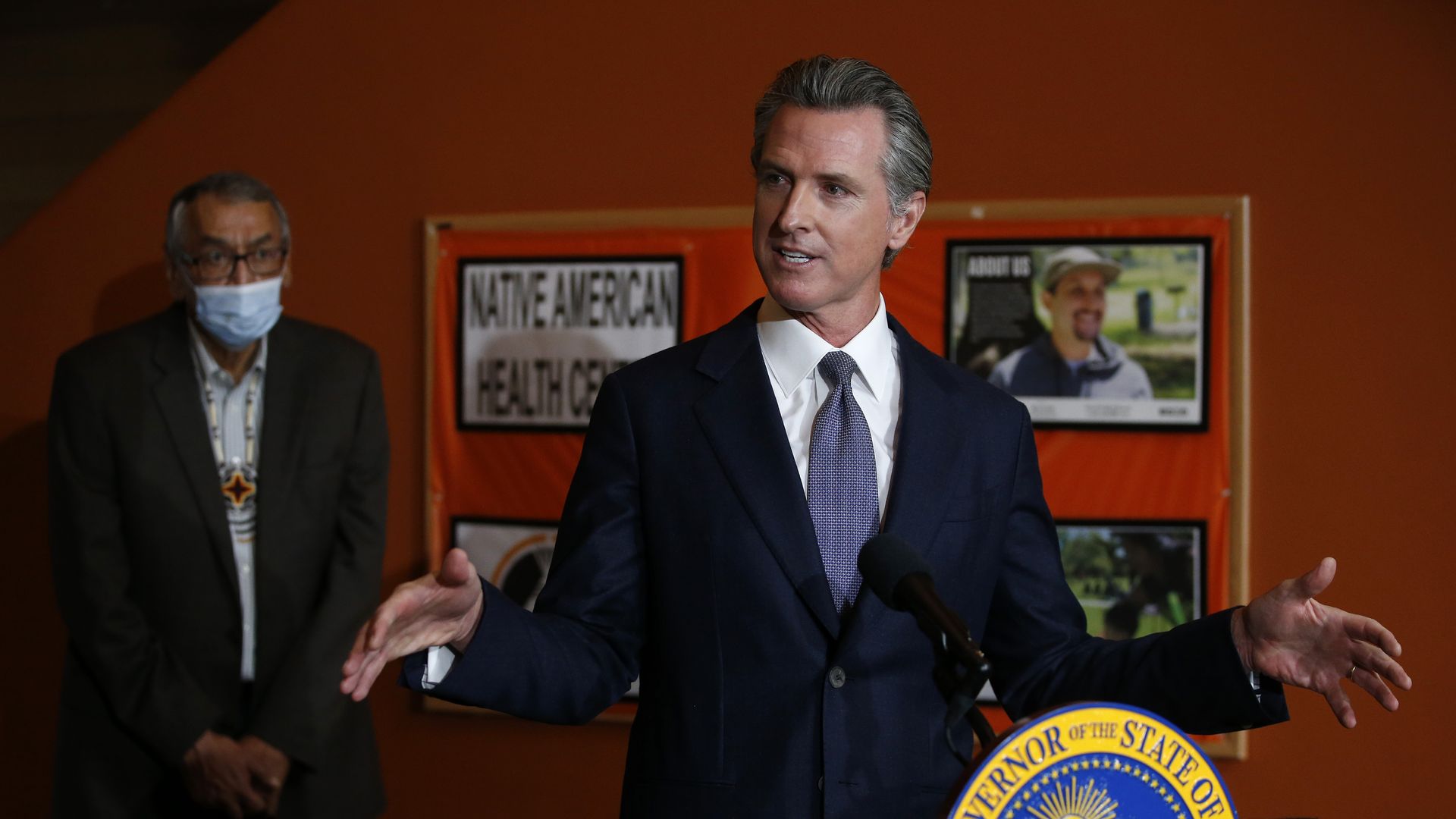 Photo of Gavin Newsom speaking from a podium while gesturing with his hands raised