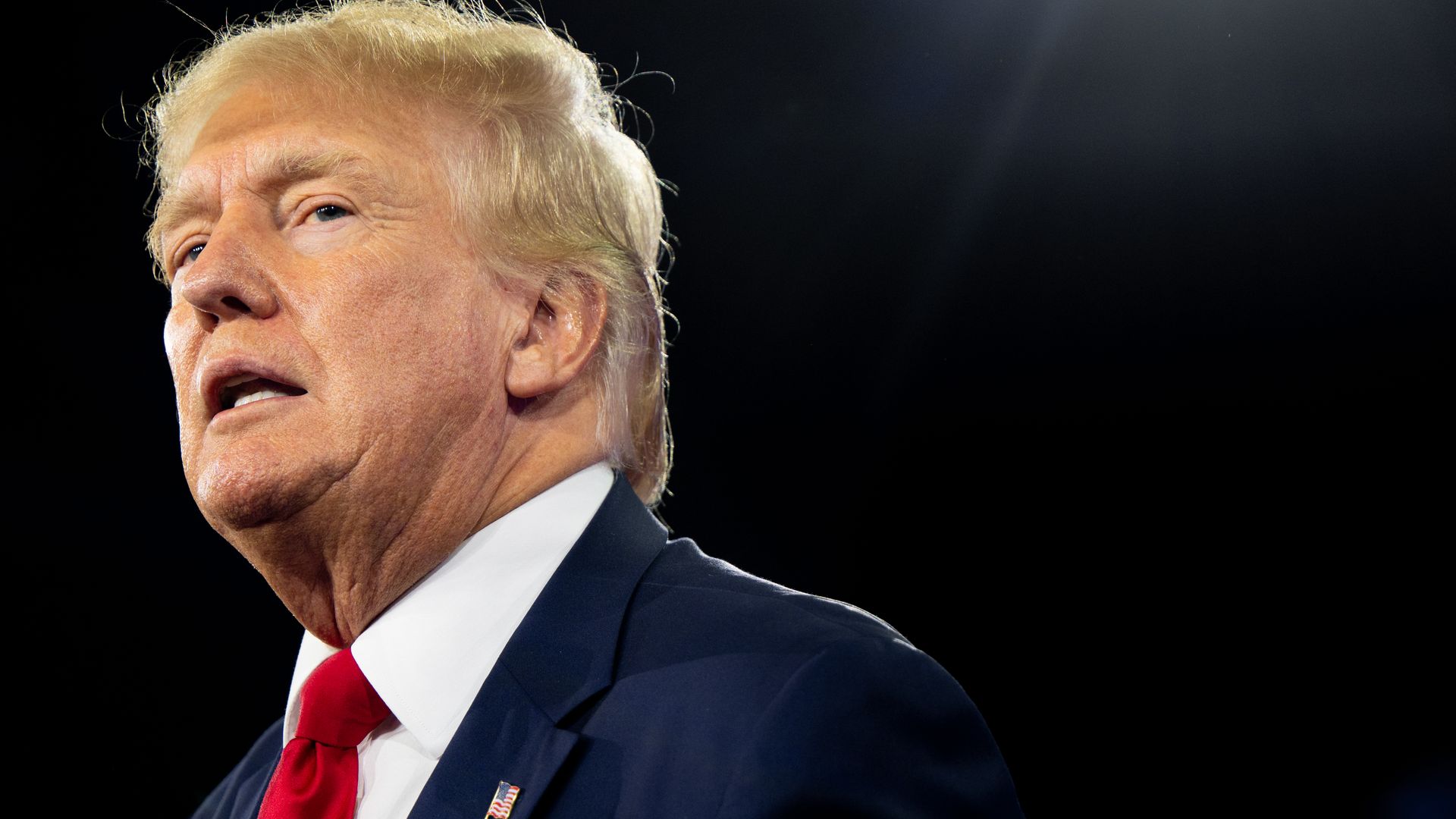 Donald Trump stands in front of a black background.