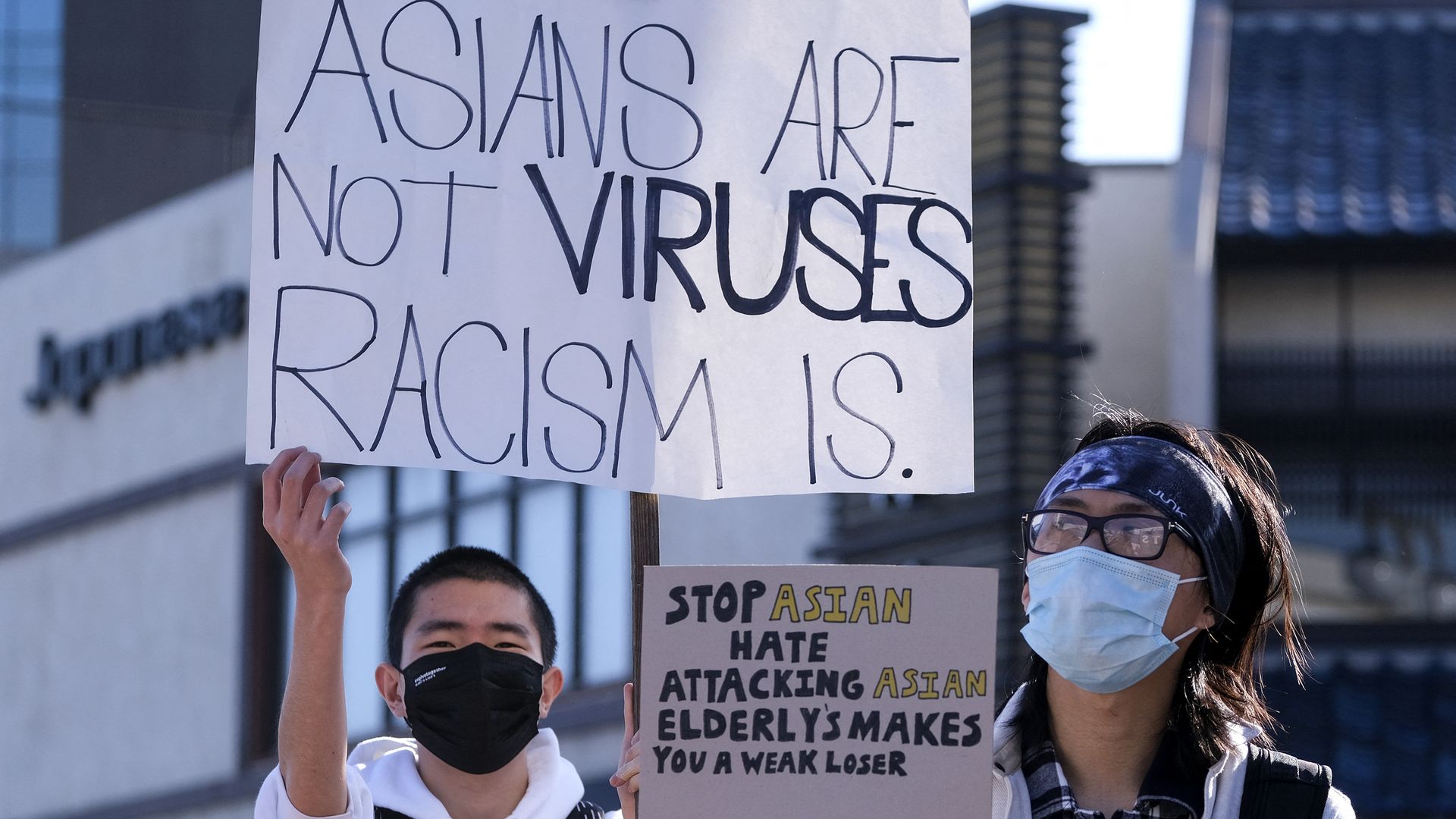 Photo of two protesters holding up signs protesting anti-Asian hate