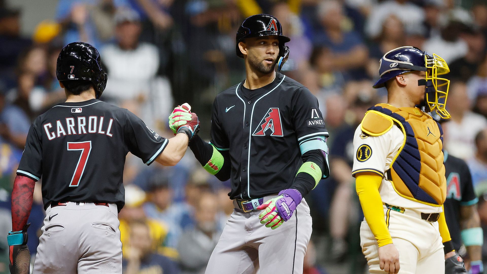 Two Arizona Diamondbacks players in black jerseys and light gray pants shake hands on the baseball field while a Milwaukee Brewers catcher looks away. 