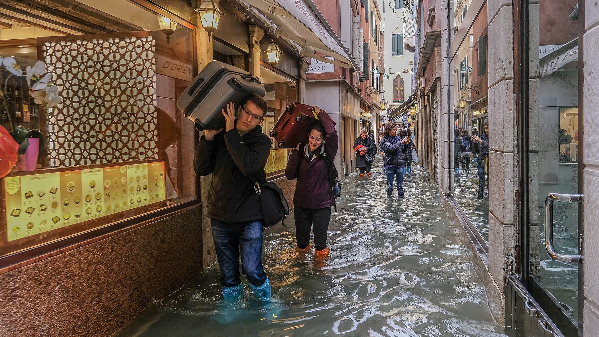 People carrying their luggage over their heads in venice due to flooding.