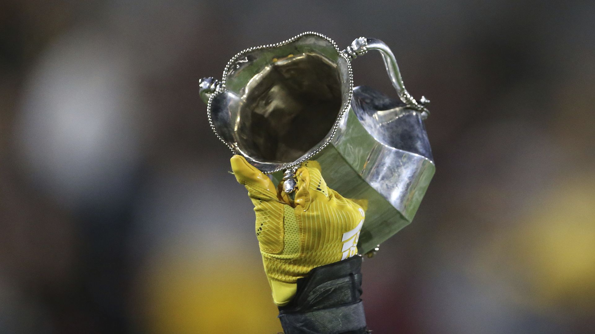 A gloved hand holding up a shiny trophy cup. 