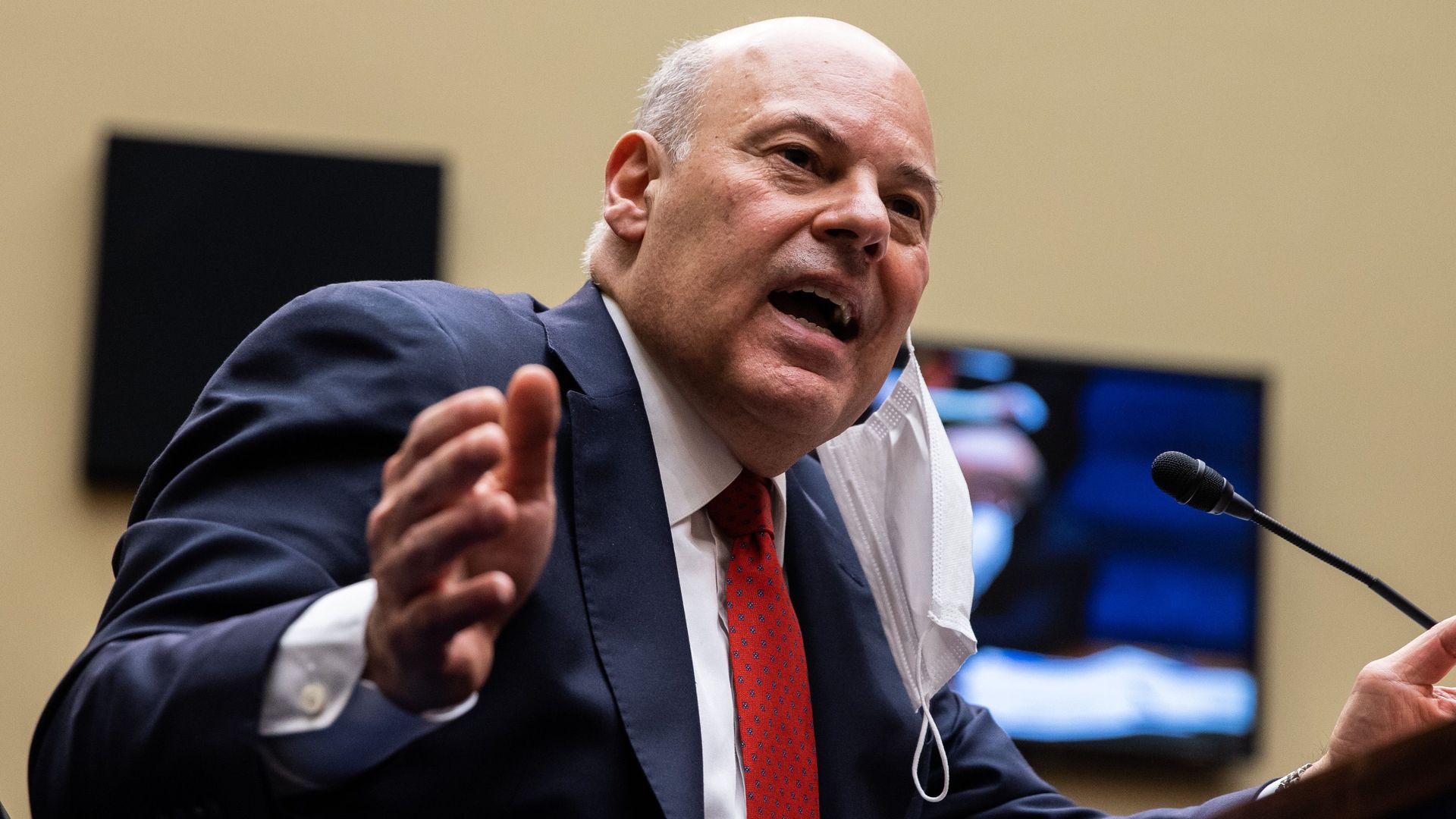 Postmaster General DeJoy wears a suit and gestures while talking