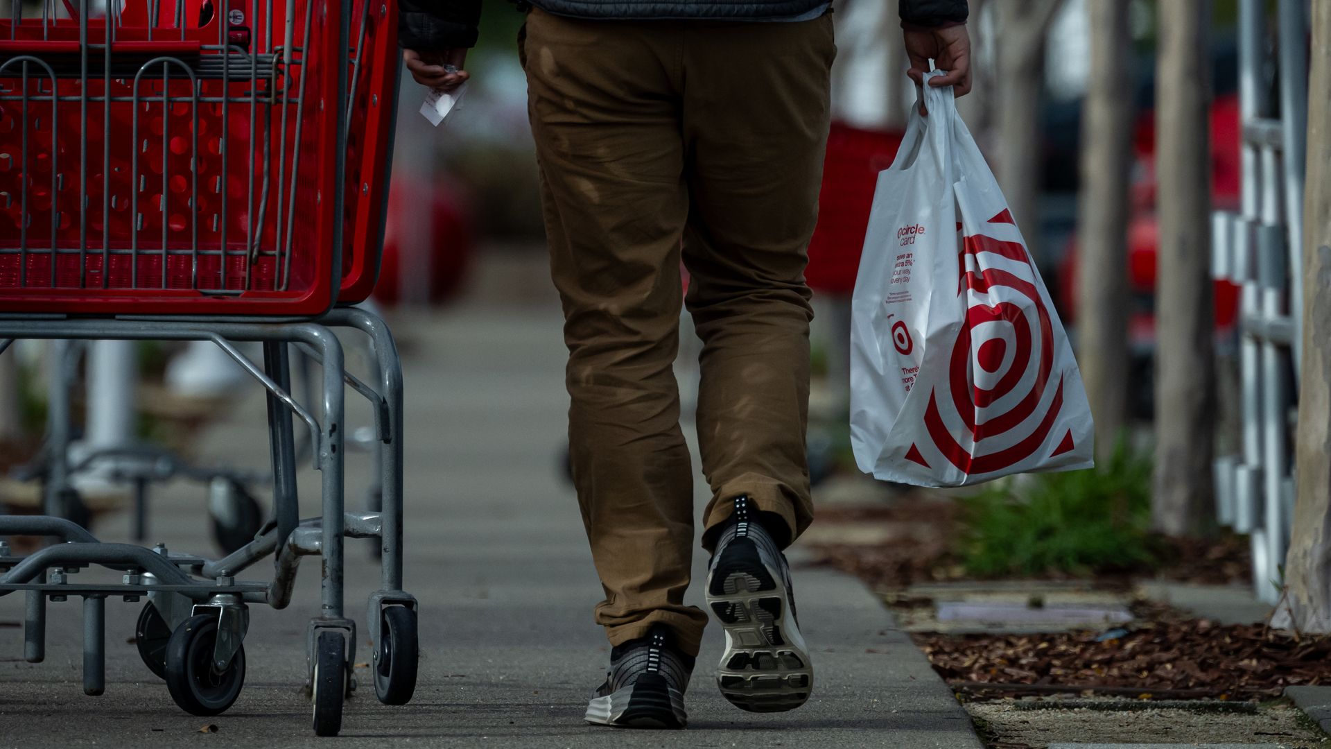 A shopper carries a bag outside a Target store and is next to a store shopping cart. 