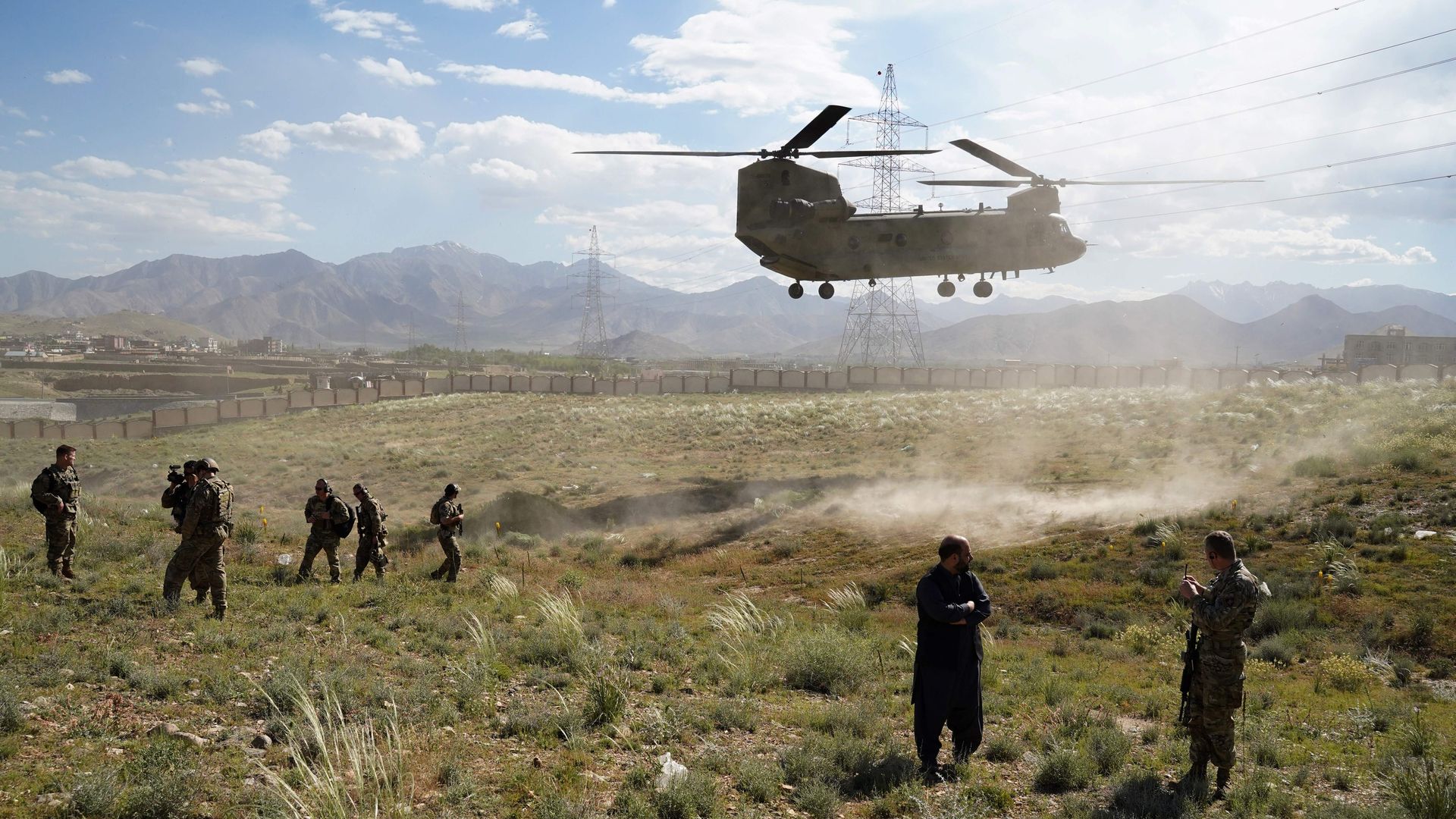 Photo of a helicopter landing on a field as a handful of soldiers watch