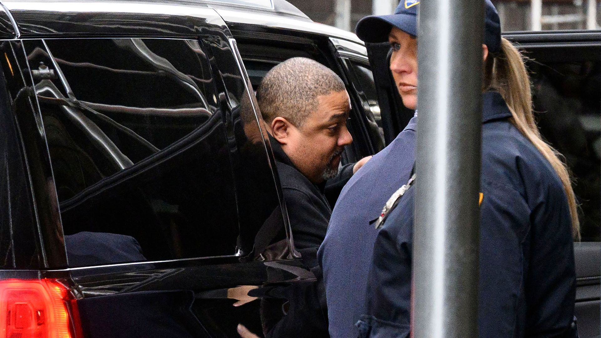 Manhattan District Attorney Alvin Bragg steps out of a black suburban onto a sidewalk covered by scaffolding.