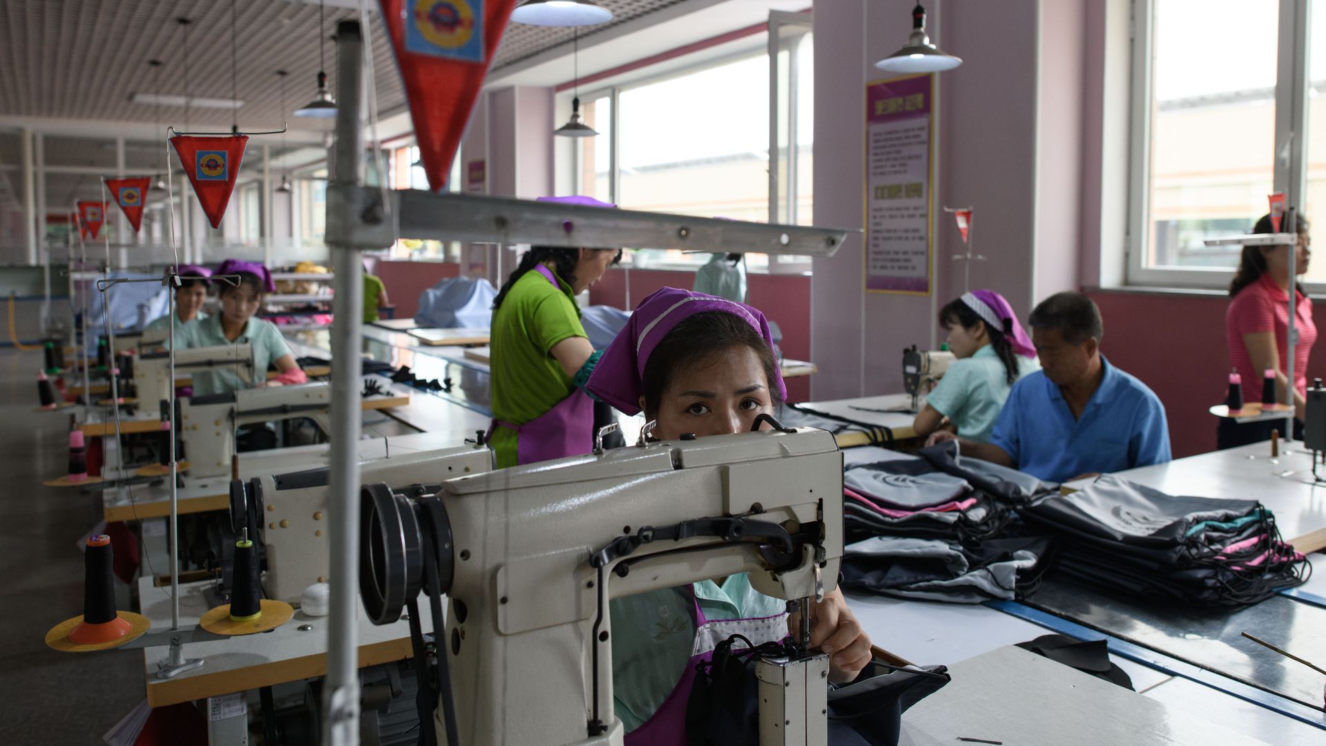 A North Korean woman with a pink bandana looks at the camera over a sewing machine in a factory
