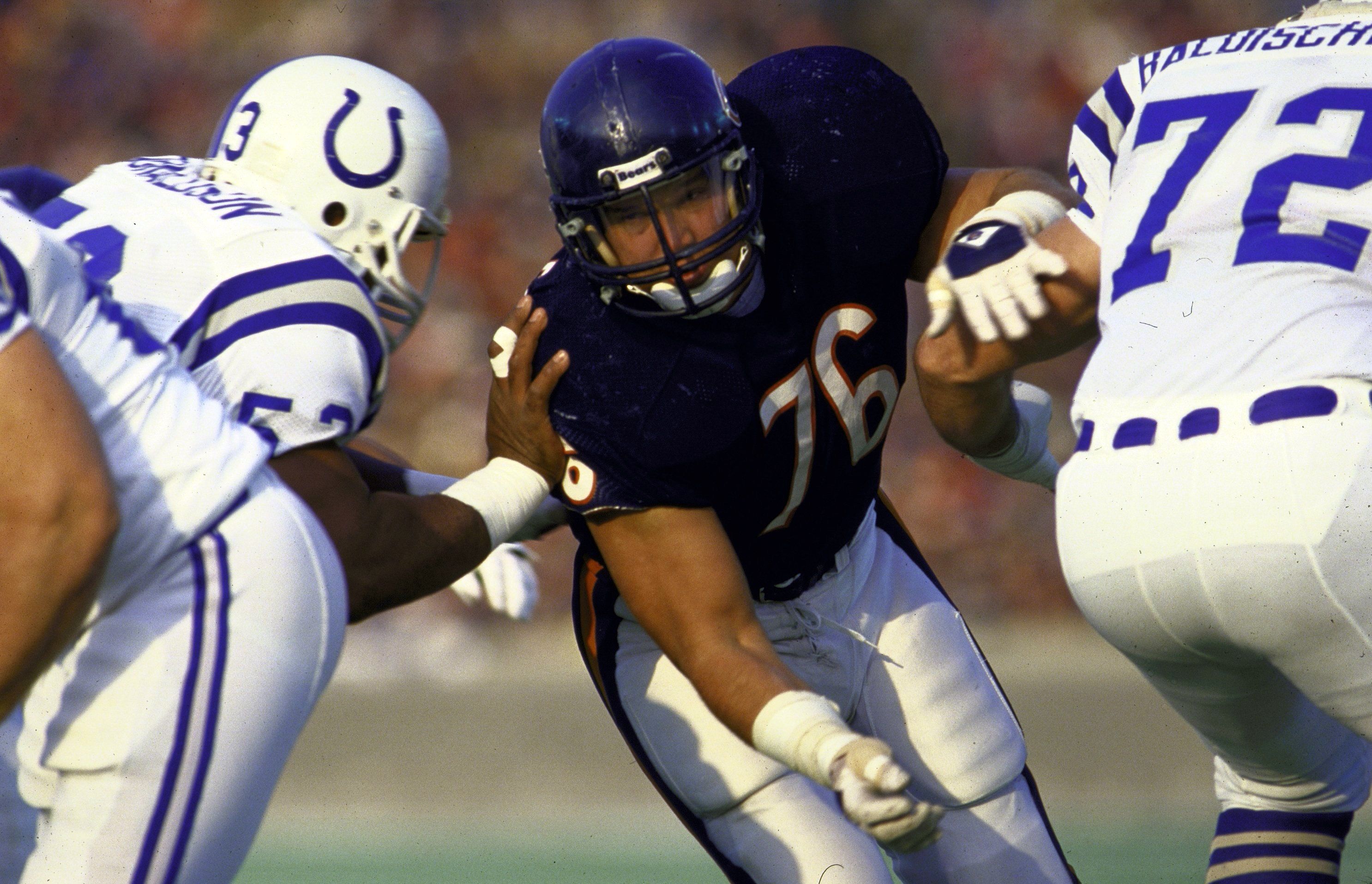 American football players in action, including one in a dark jersey number 76 and two in white jerseys with blue horseshoe logos and numbers 53 and 72, engaged in a close play.