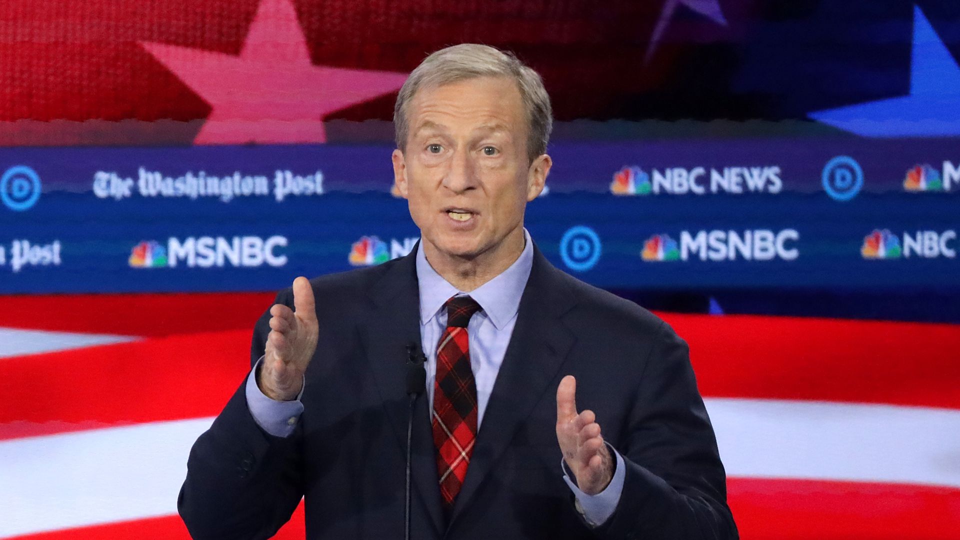 Tom Steyer speaks into a microphone with a backdrop that has the logos of NBC News, MSNBC and the Washington Post. 
