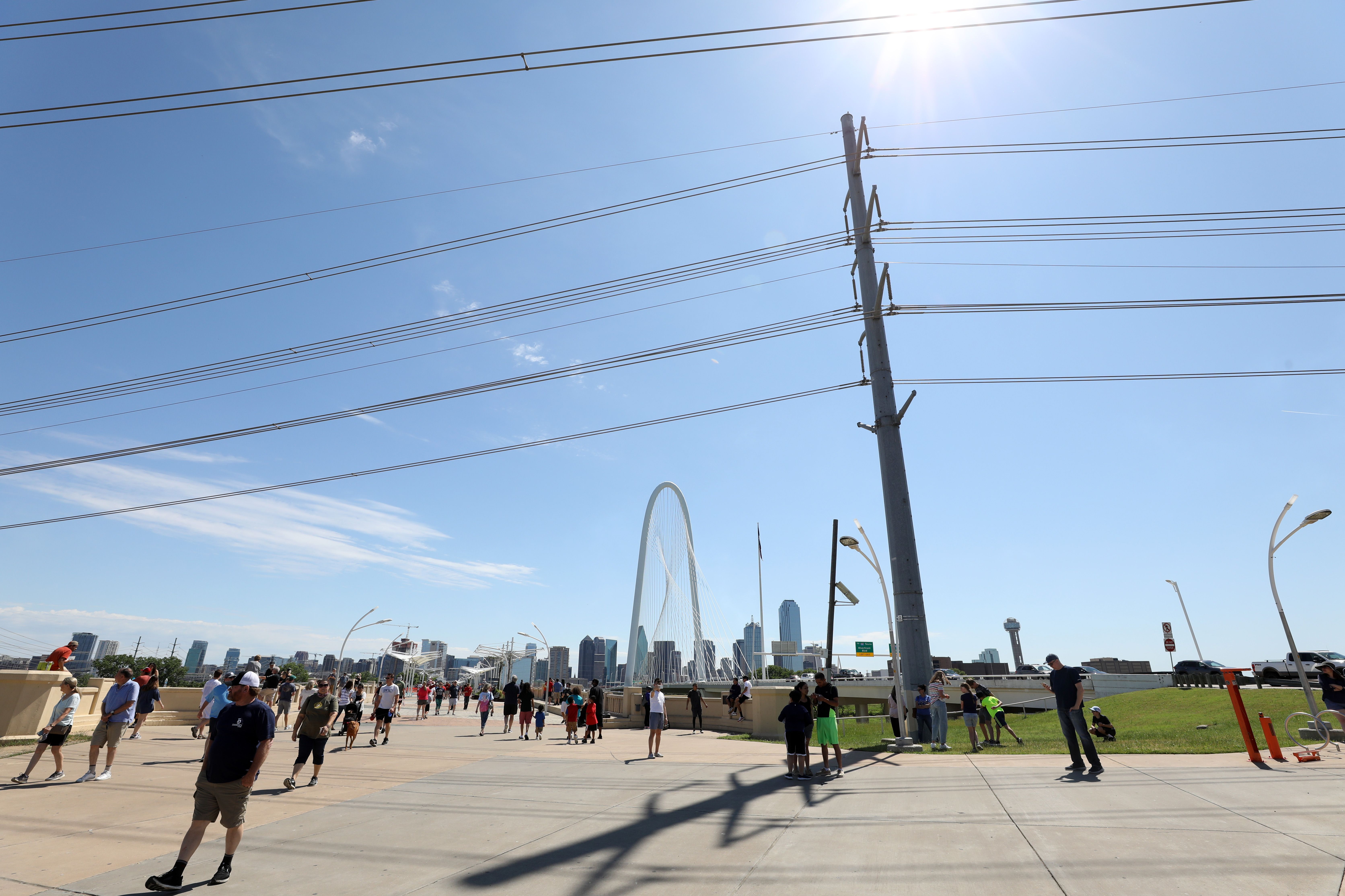 People gather on a pedestrian bridge in front of the Dallas skyline