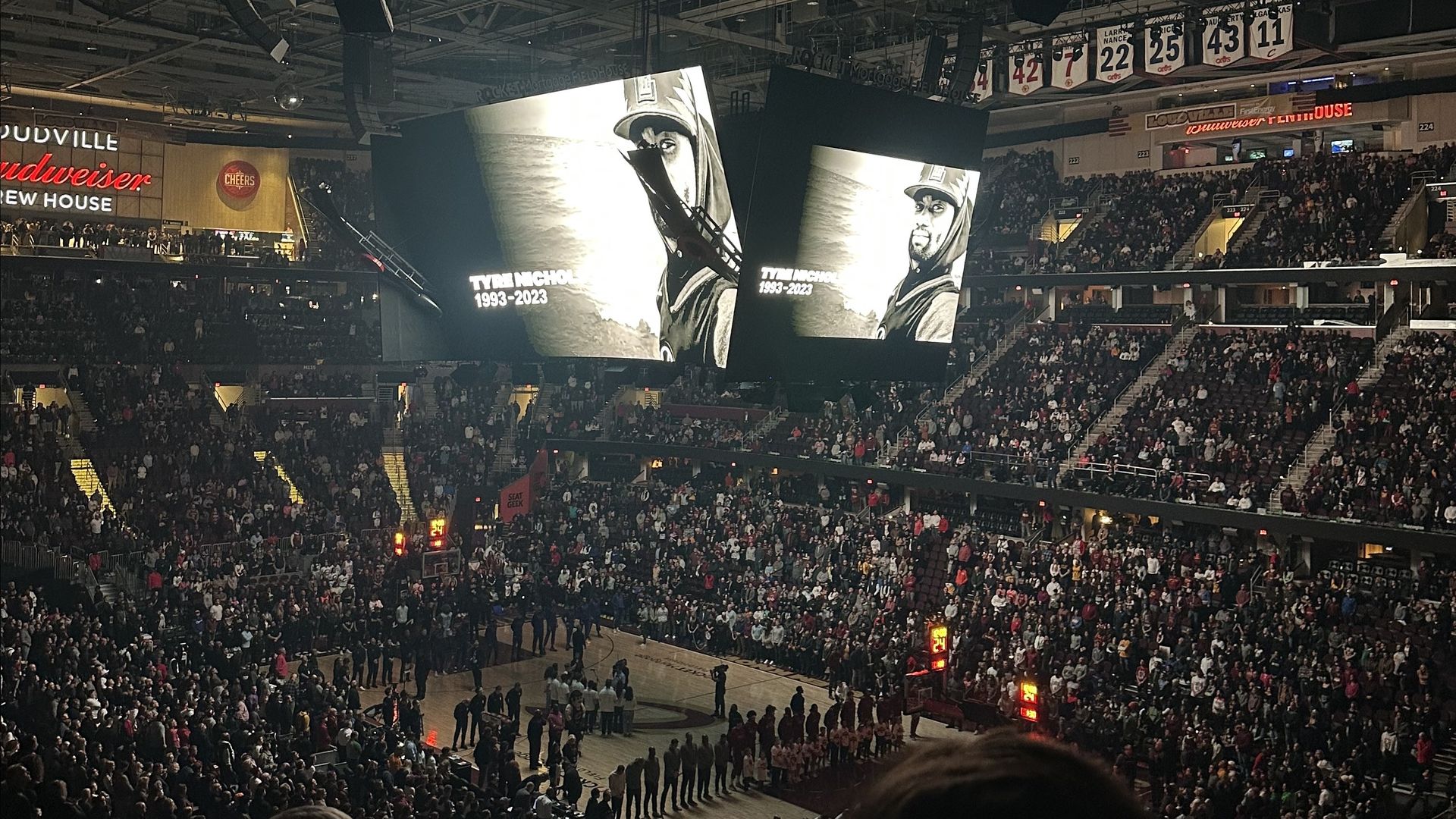 Thousands of fans stand inside a basketball arena as a tribute to Tyre Nichols shows on a jumbotron.