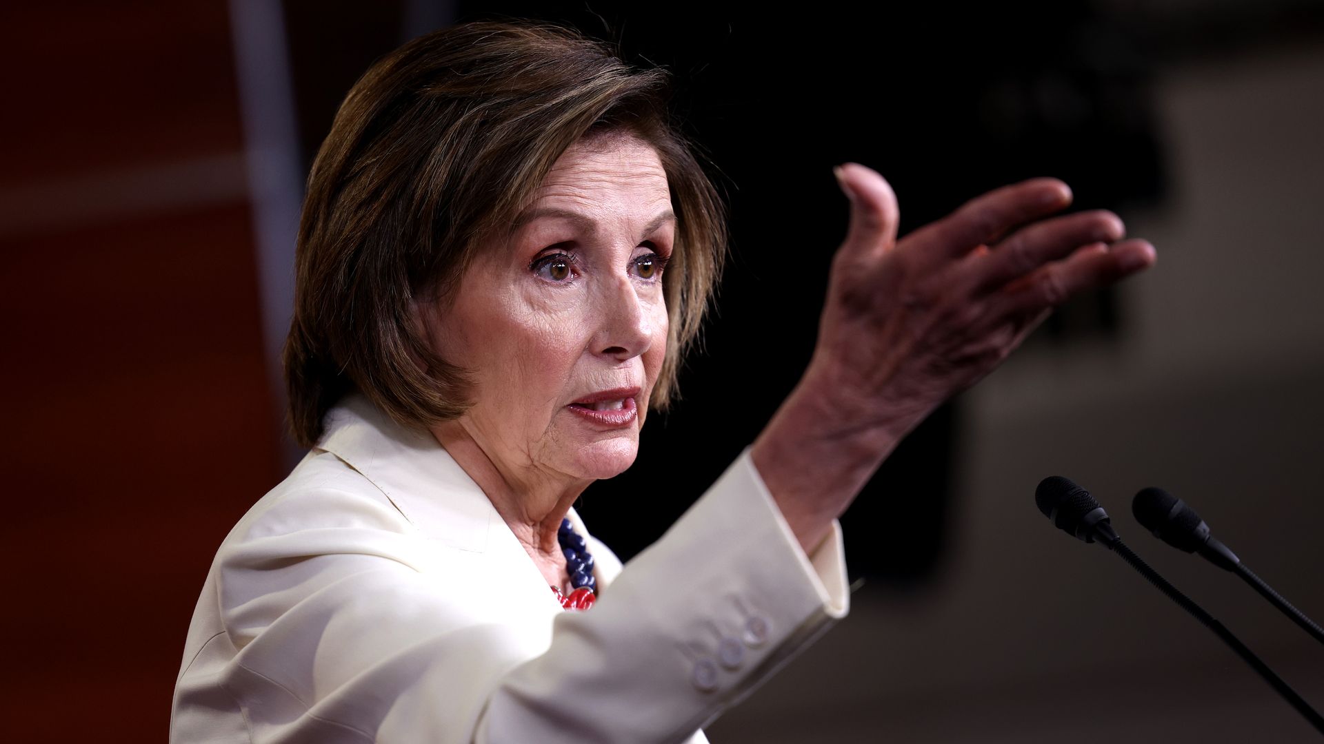 Photo of Nancy Pelosi wearing a white suit and gesturing while speaking