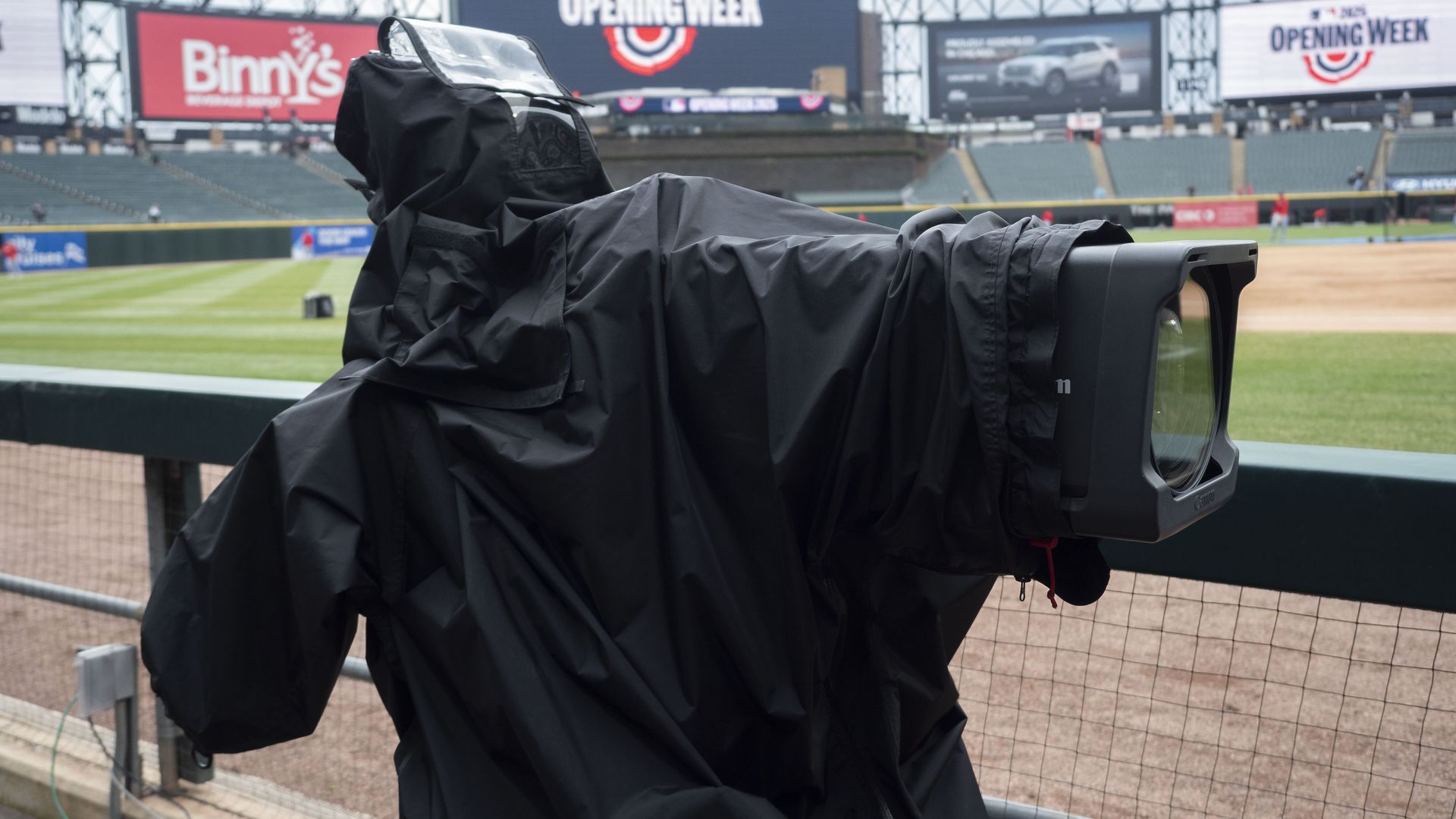 Photo of a television camera with a tarp over it at a baseball stadium. 