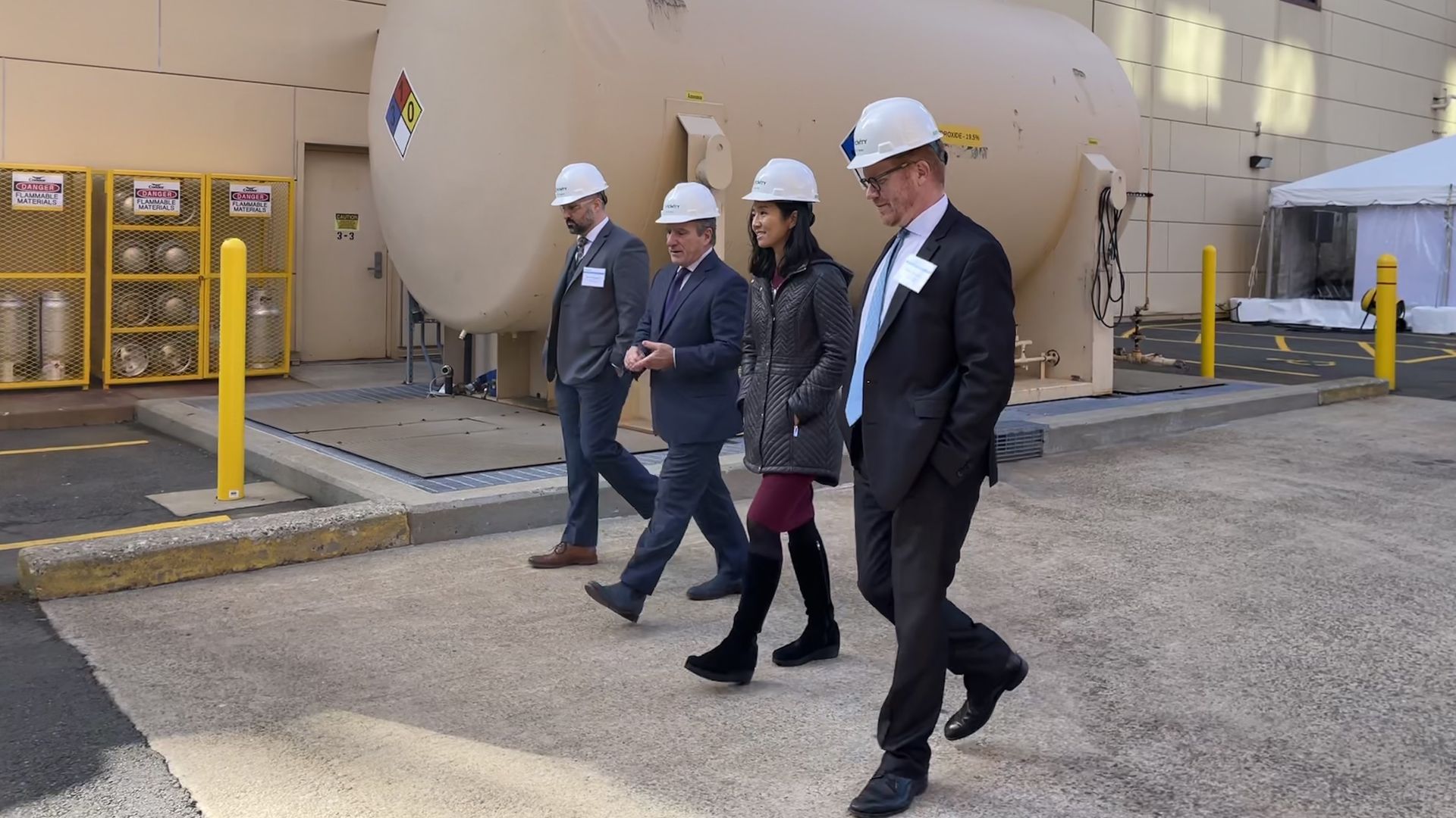 Vicinity executives walk beside Boston Mayor Michelle Wu, all of them wearing white hard hats, as they head into the company's Cambridge steam plant.