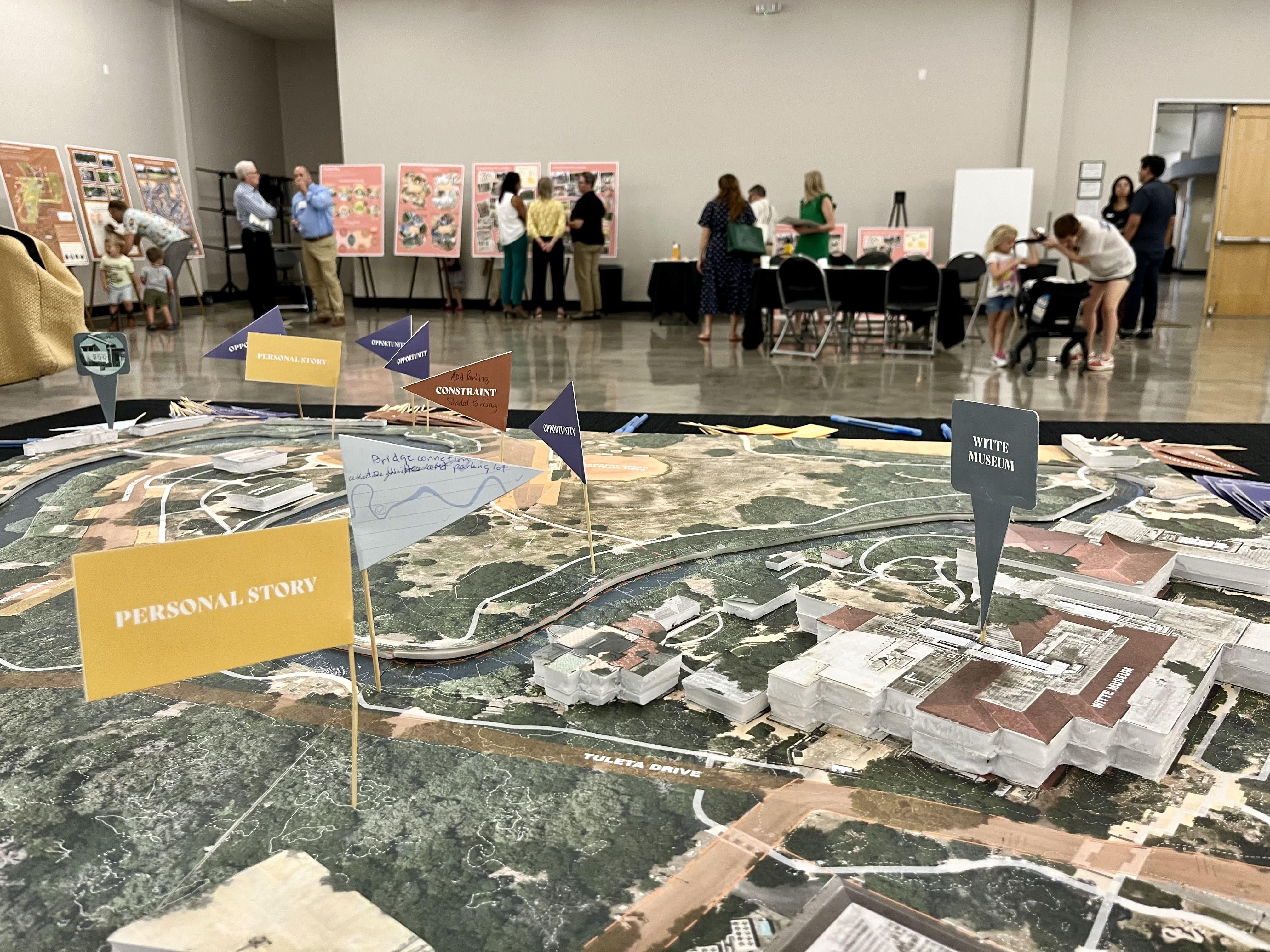A 3D map of Brackenridge Park has flags showing personal stories, with people looking at slides in the background.