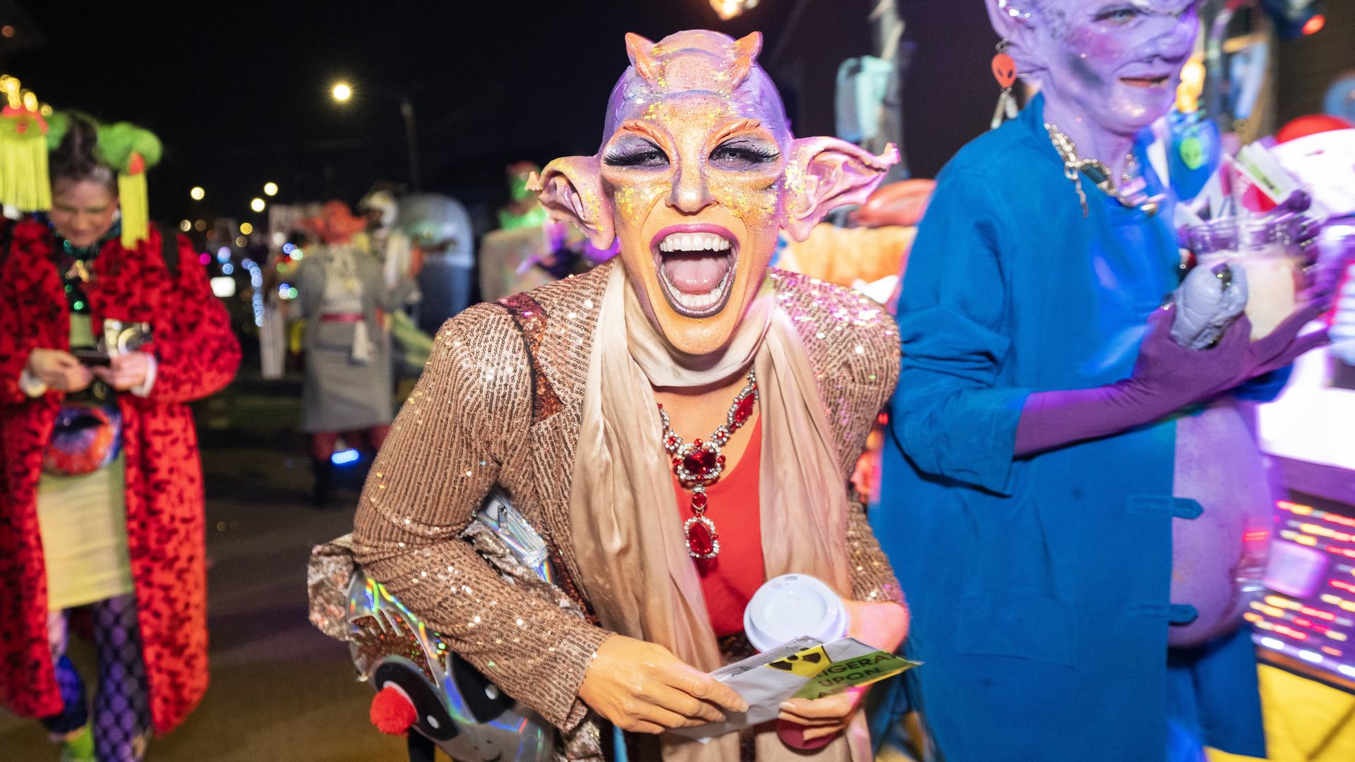 A person dressed as an orange and purple elven-styled alien grins broadly toward the camera.