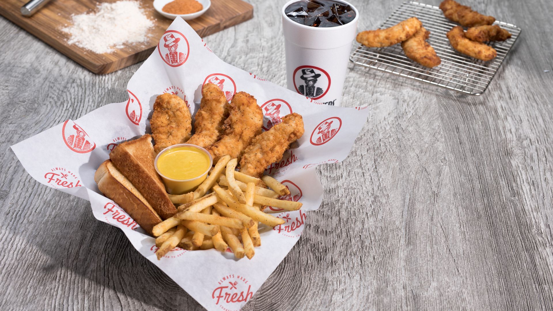 A plate of four chicken tenders with fries, toasted bread and a sauce with a drink. 