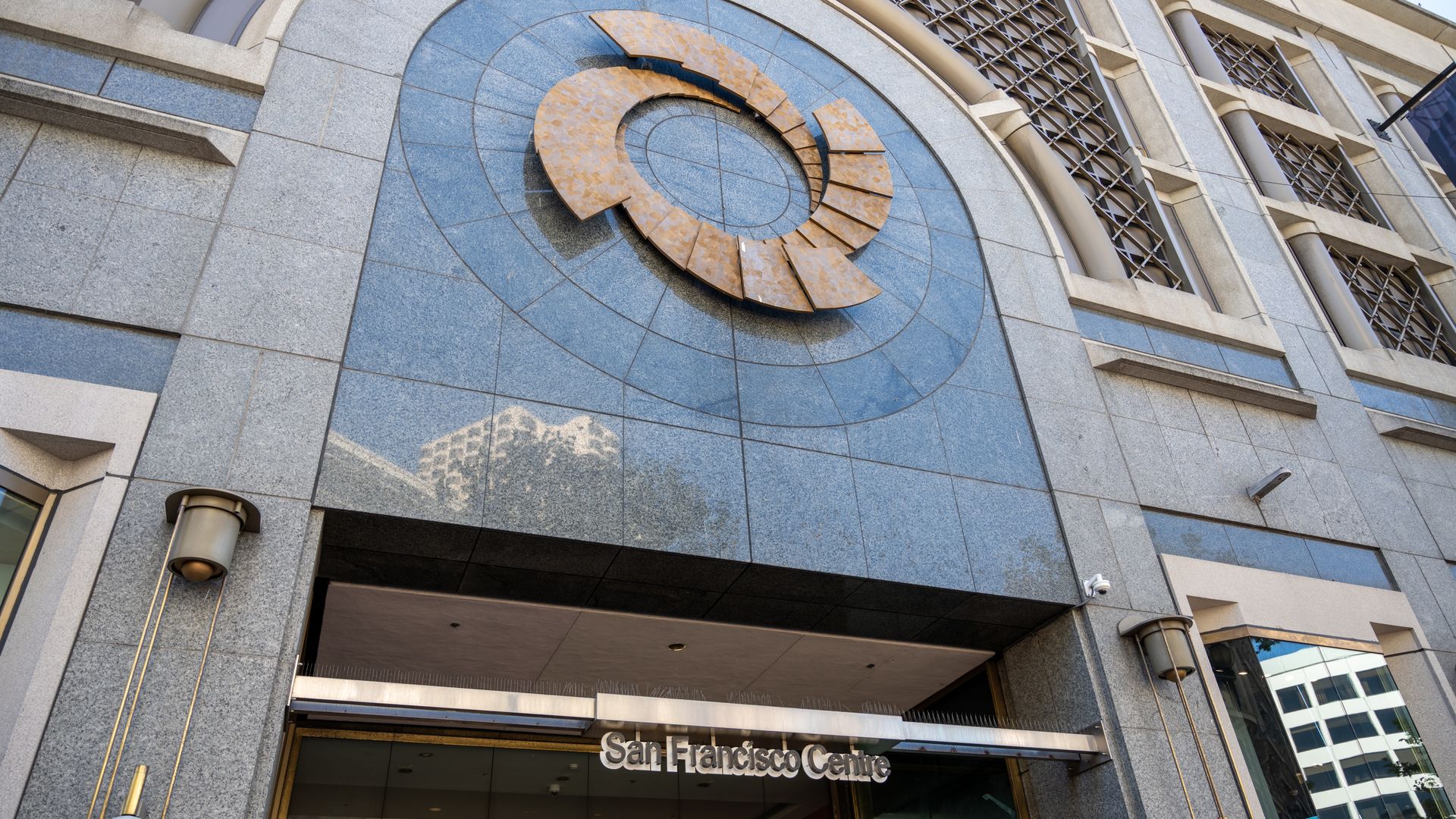 Entrance of the San Francisco Centre with blue stone facade, circular bronze art above doorway, and metal signage reading "San Francisco Centre".