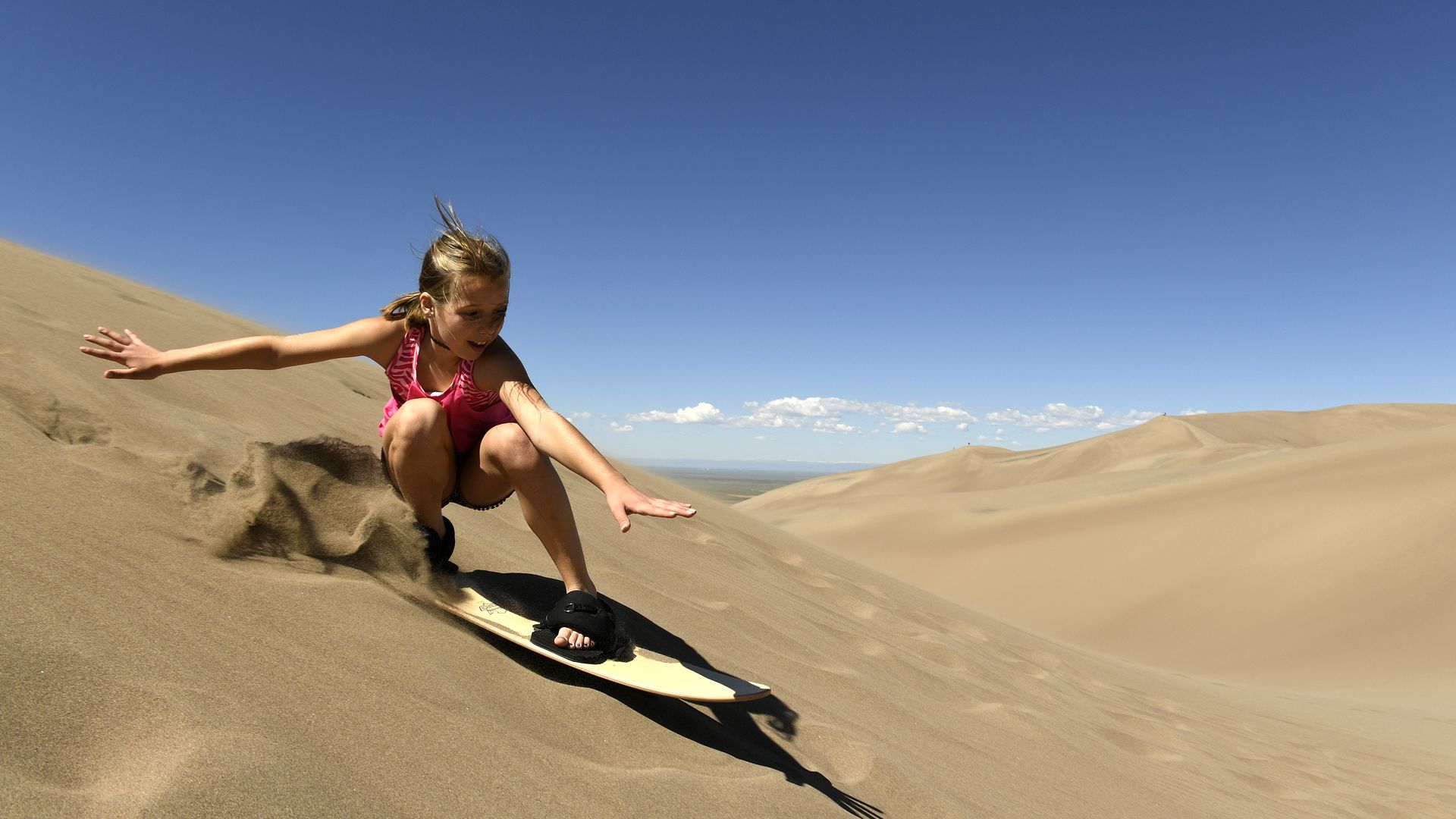 An image of a young girl surfing sand dunes.