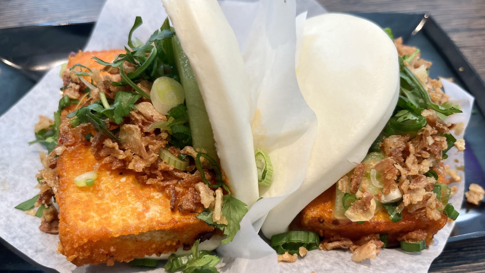 A bun is stuffed with fried tofu topped with crispy shallots and green herbs.