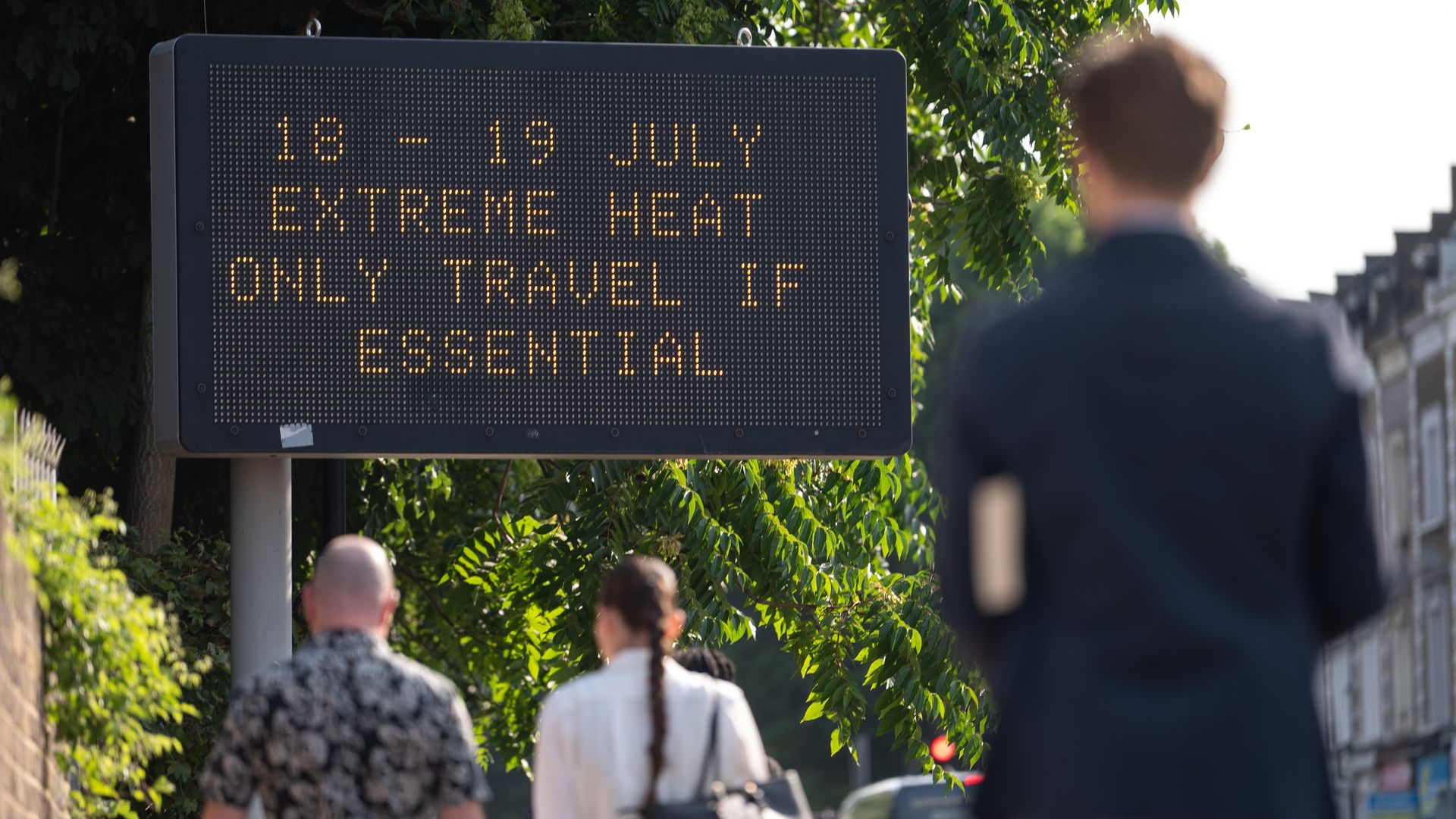 Passersby walk towards an LED sign saying "18 -19 July extreme heat only travel if essential" in the London, England.