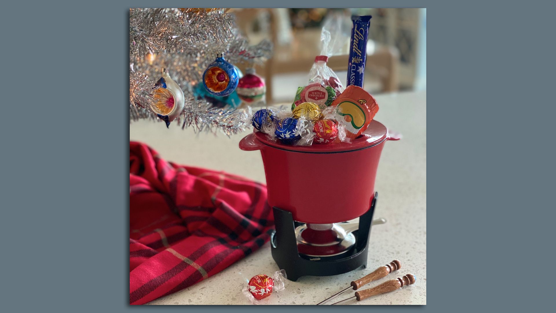 A fondue pot with assorted individual chocolates around it and a Christmas tree in the background. 