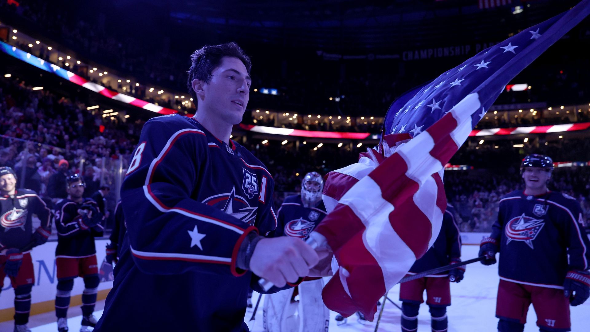 Blue Jackets defenseman Zach Werenski skates onto the ice with an American flag in hand