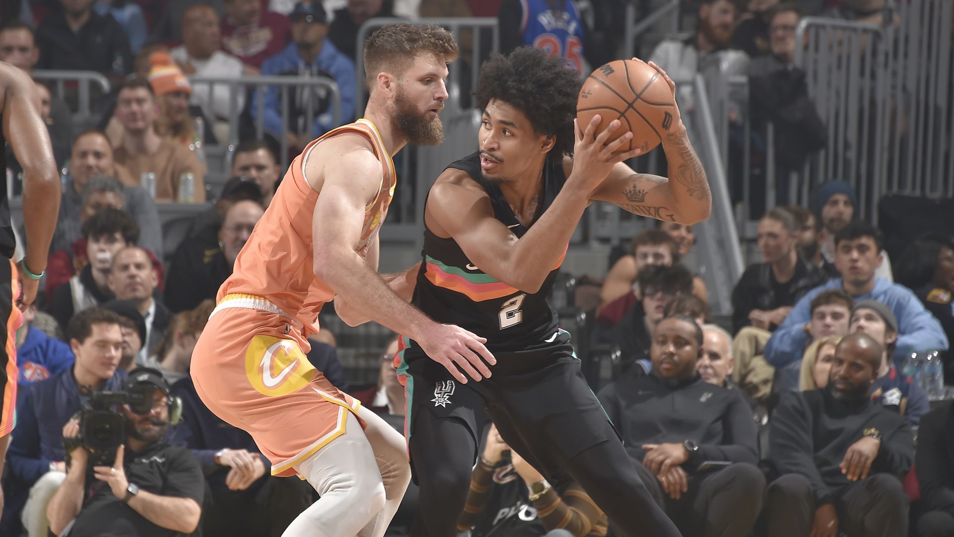 White player in salmon jersey guard black player in black jersey on pro basketball court