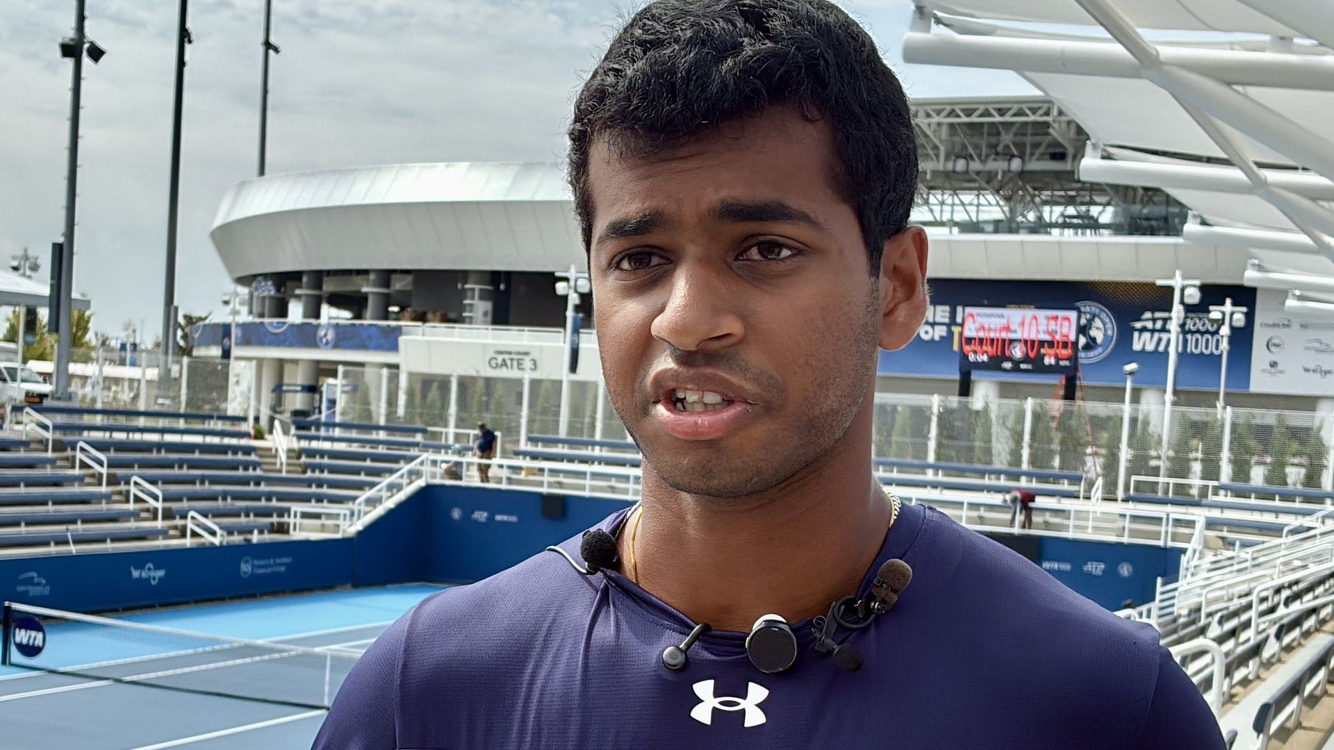 Vignesh Gogineni, wearing his practice gear from Yale, talks during a preview day at the Cincinnati Open. Vignesh is standing in front a sunken court at the Lindner Family Tennis Center.