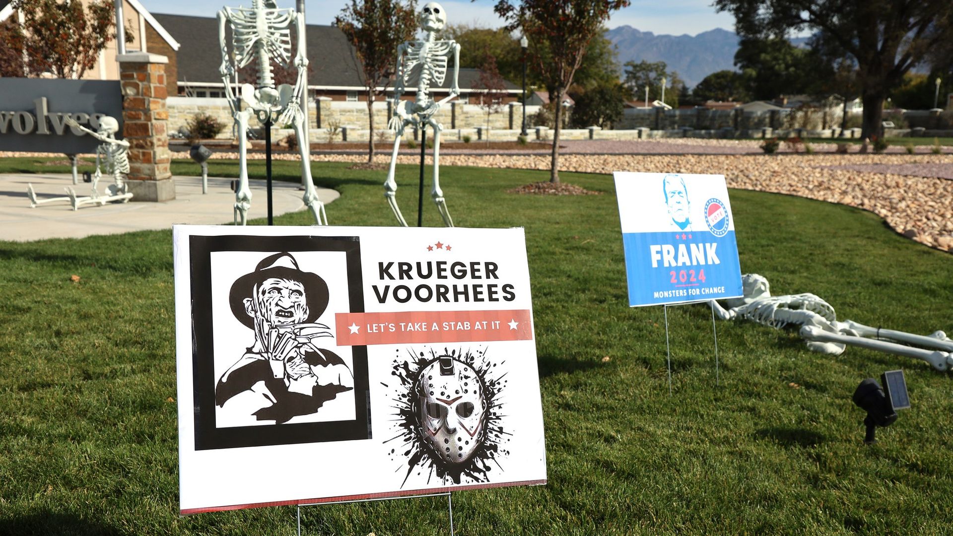 A fake election sign reads "Kreuger Voorhees: Let's take a stab at it" in a park surrounded by plastic skeletons.